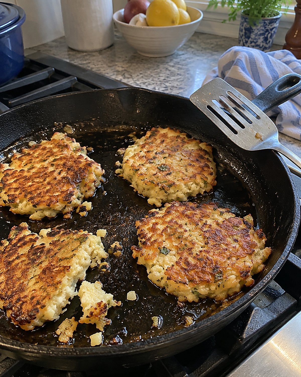 Uneven mashed potato cakes brown in a cast-iron skillet, with a spatula resting nearby.