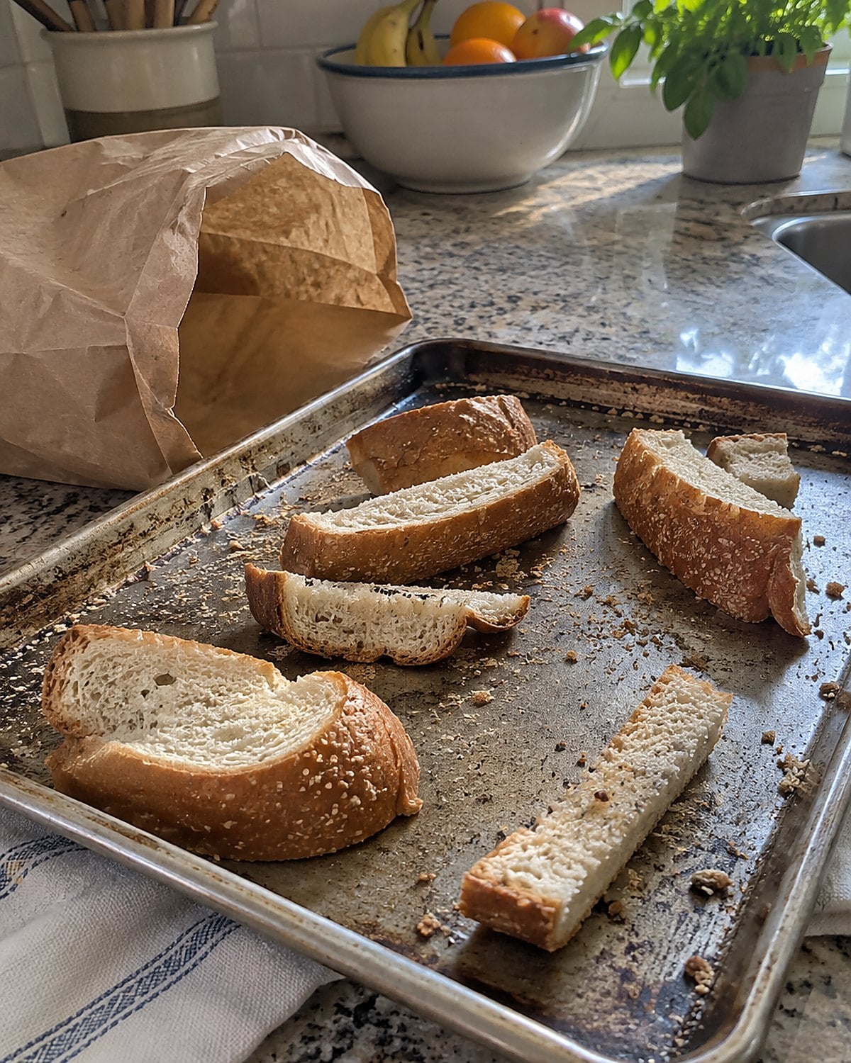 Uneven bread heels rest on a baking sheet beside an open paper bag.