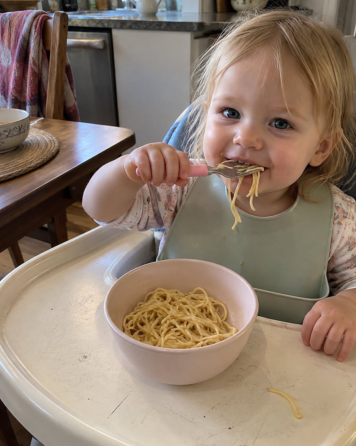 A small bowl of buttered noodles sits on a grandchild’s high-chair tray.