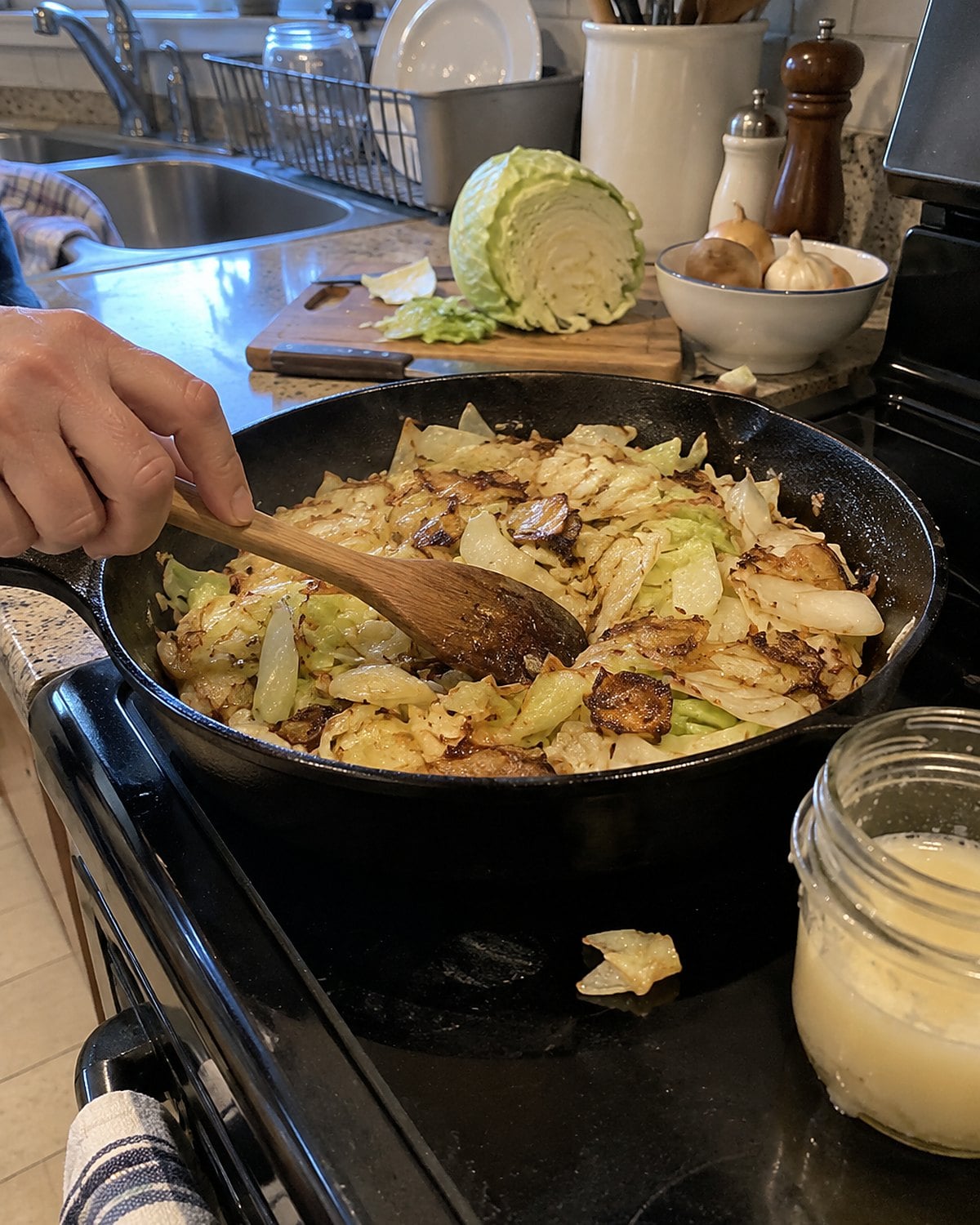 Rough-cut cabbage browns in a skillet beside a small jar of bacon drippings.