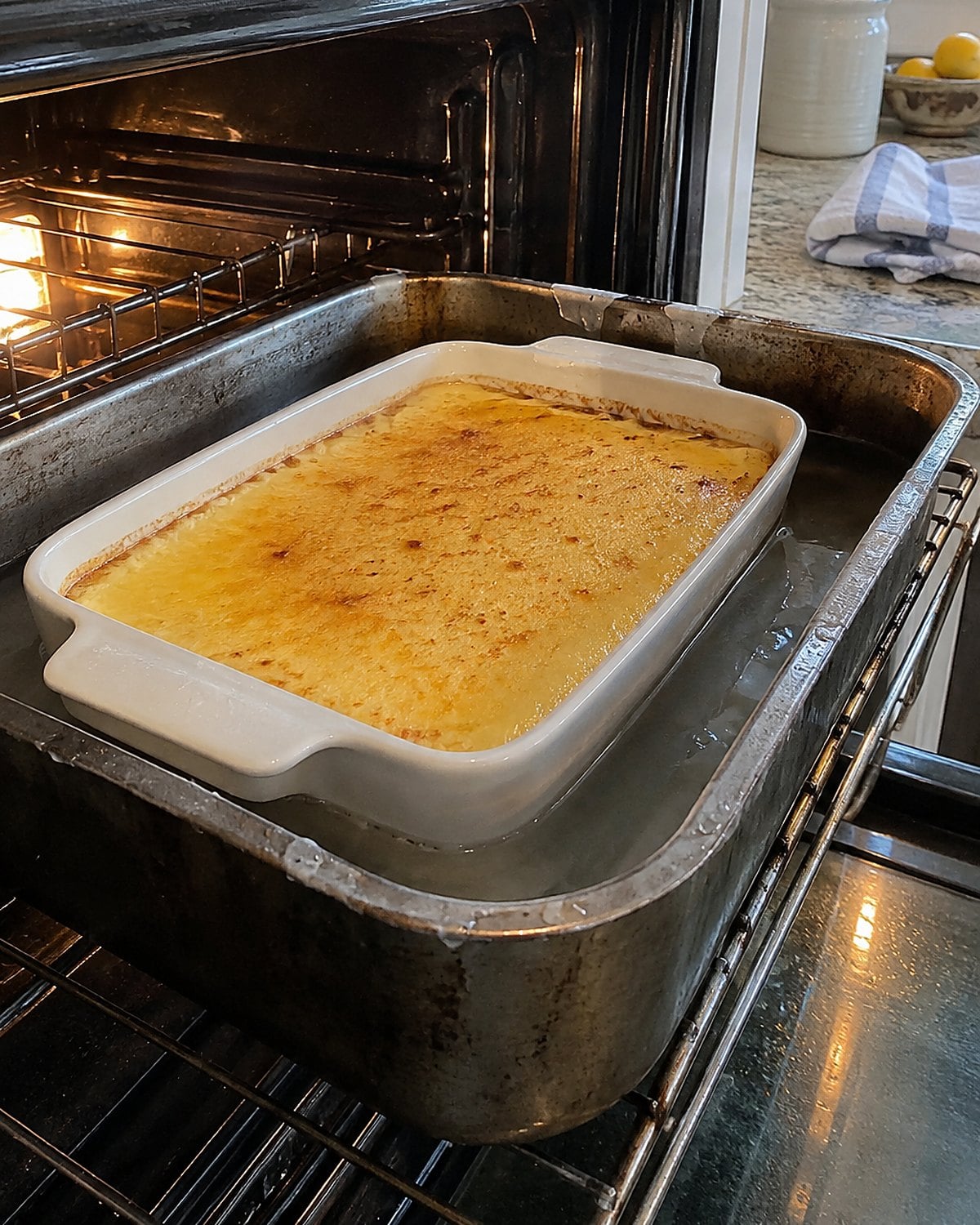 A custard dish sits inside a larger pan of water on an oven rack.