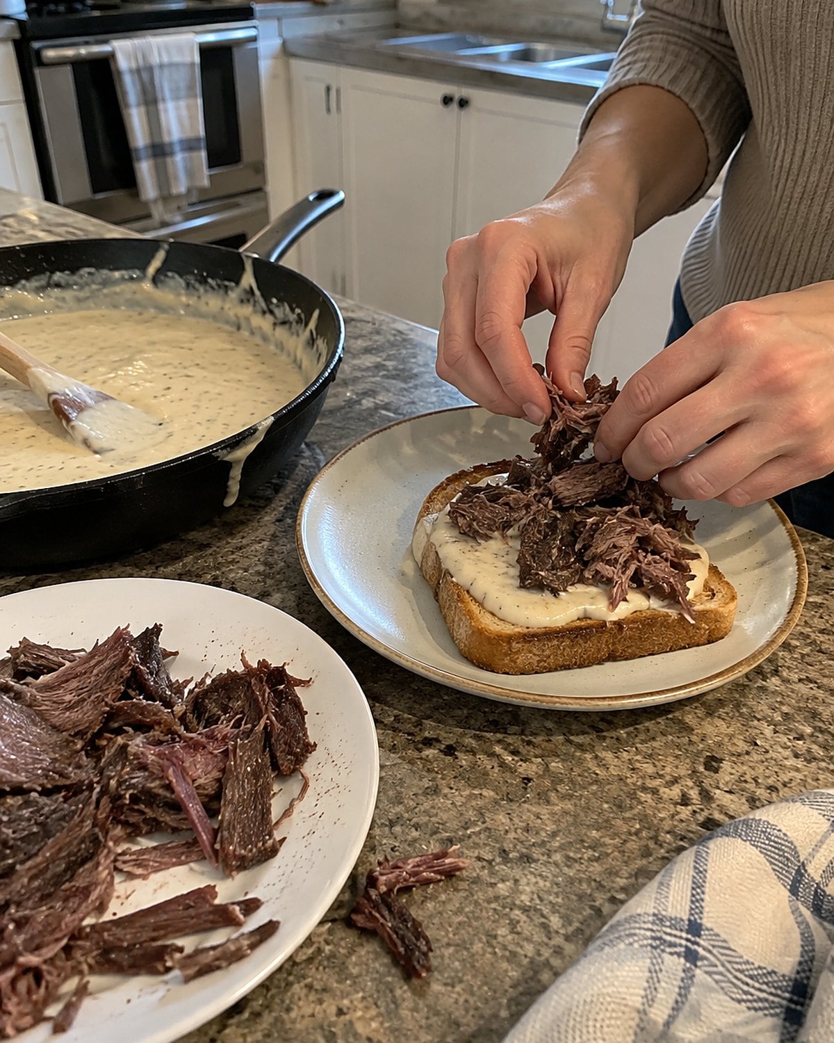Torn pieces of dried beef sit beside a skillet of white sauce and a slice of toast.
