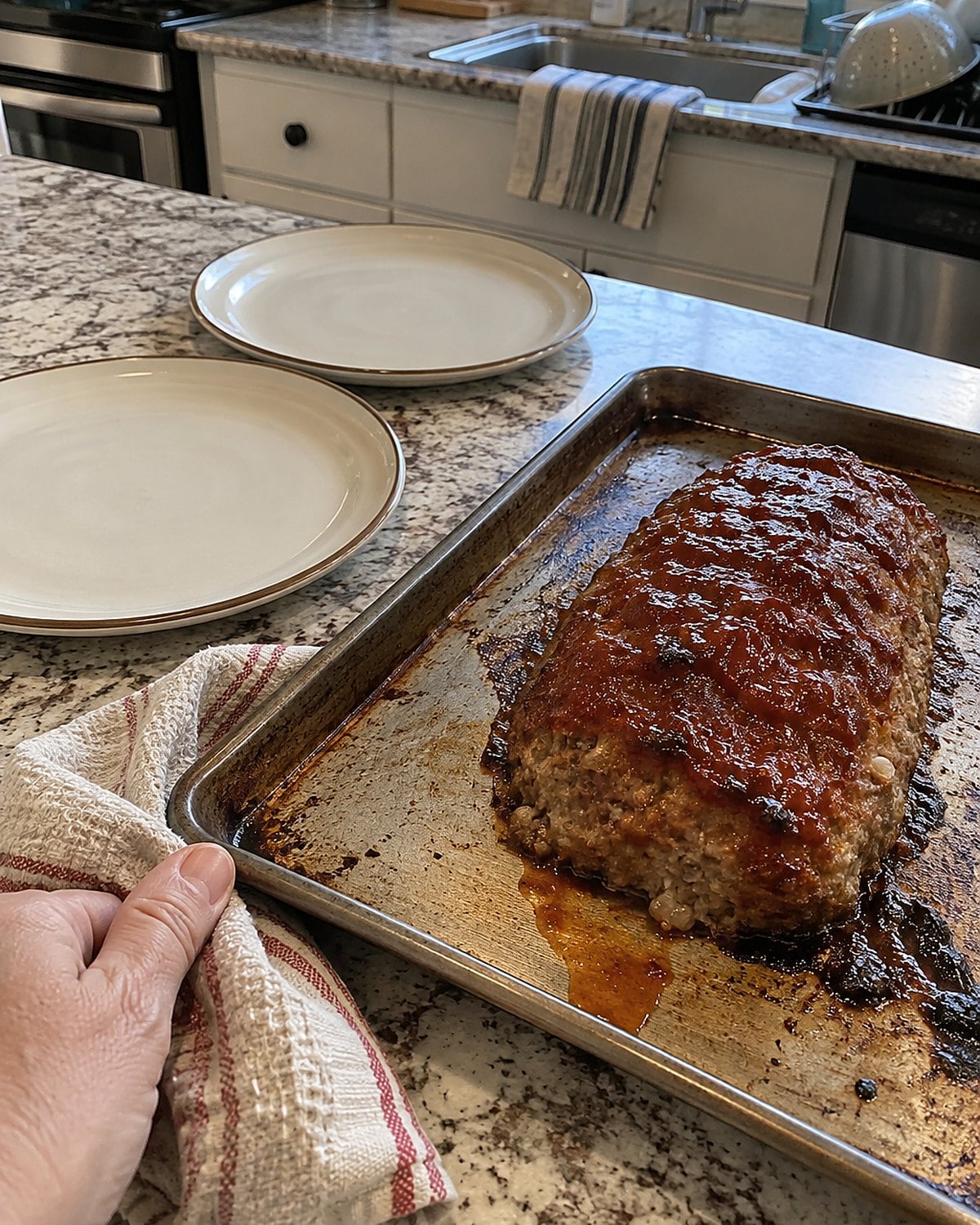 A small meatloaf sits on a baking sheet beside two empty dinner plates.