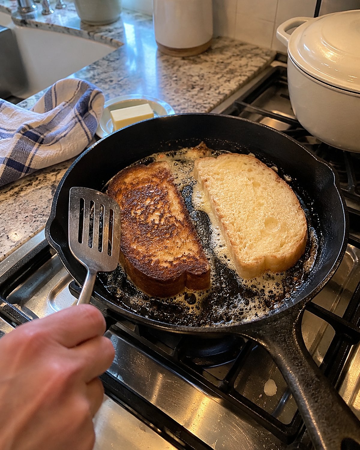 Two bread heels brown unevenly in butter in a cast-iron skillet on the stove.
