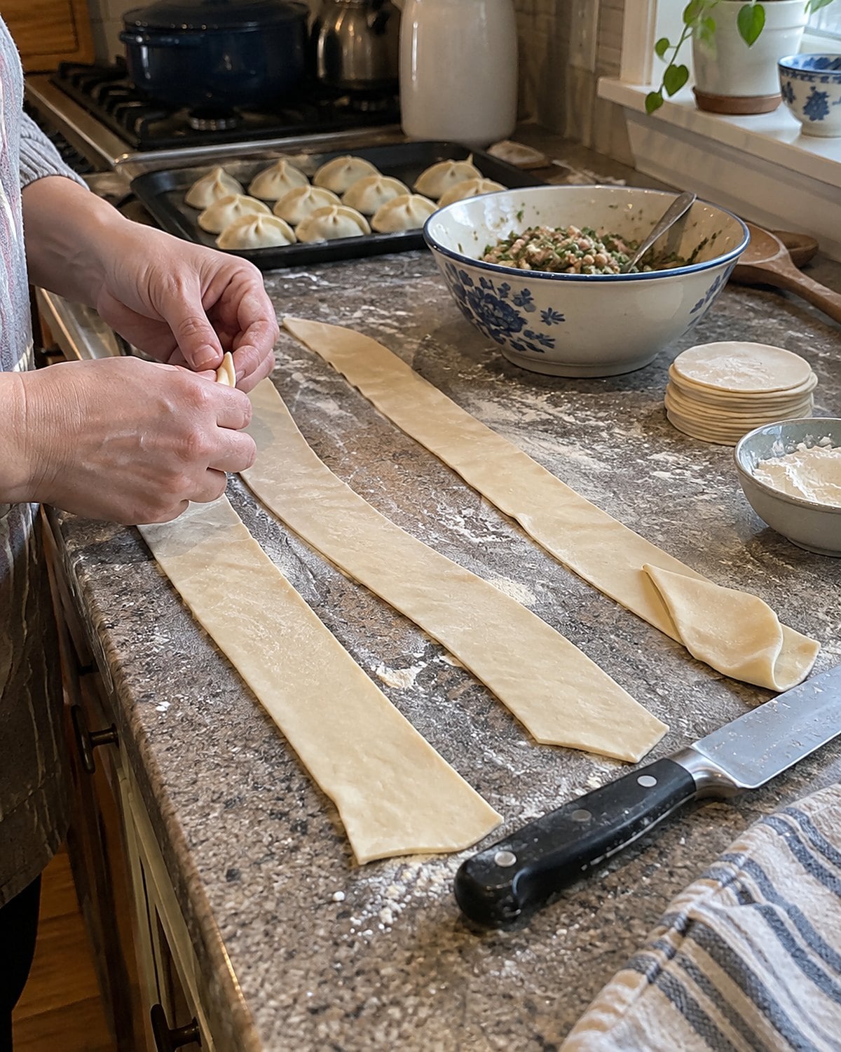 Strips of rolled dumpling dough rest on a floured counter beside a knife.
