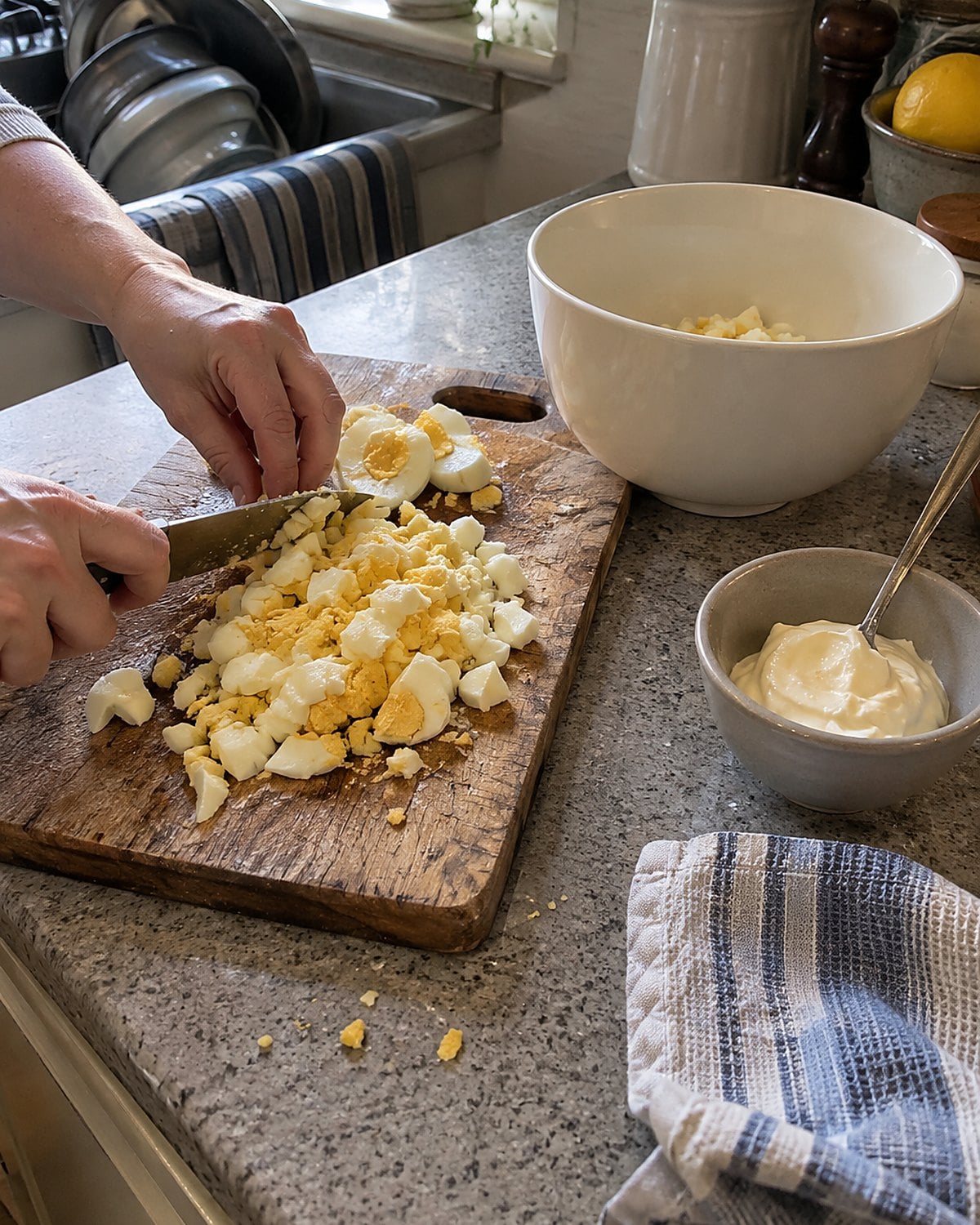 Chopped boiled eggs lie on a cutting board beside a bowl and a spoonful of mayonnaise.