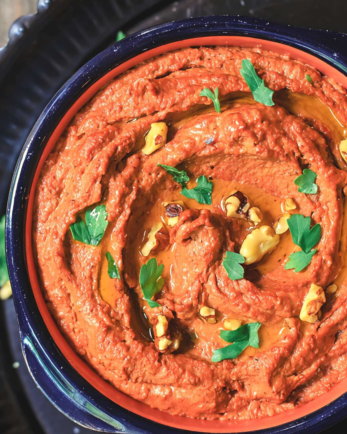 A bowl of roasted red pepper muhammara dip garnished with olive oil and chopped walnuts, perfect for vegan Thanksgiving appetizers.