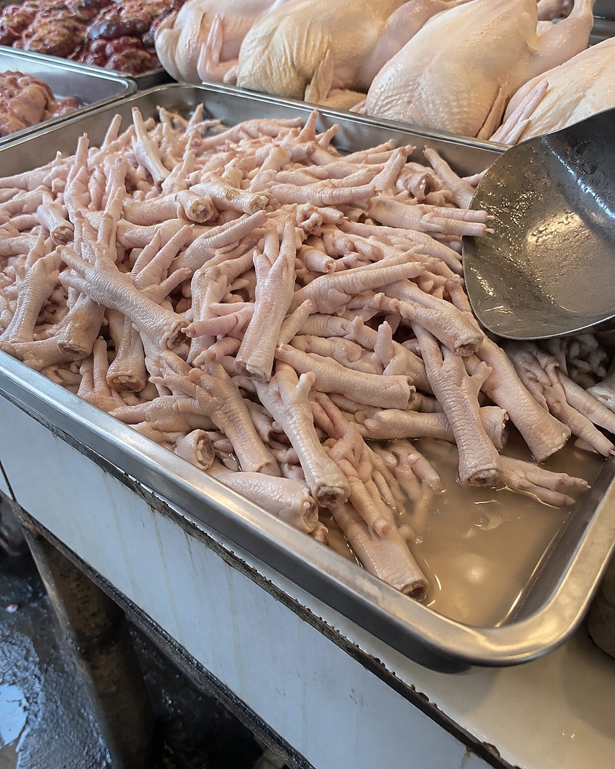 Cleaned chicken feet lie in a market stall tray beside whole chickens.
