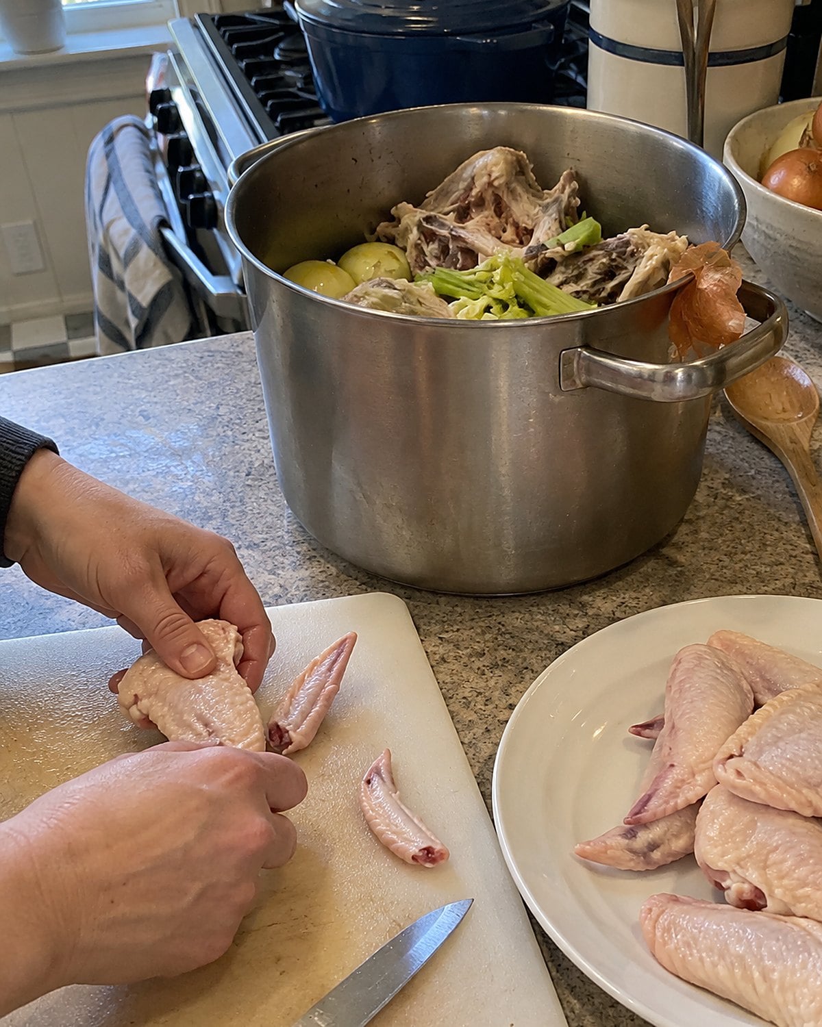 Trimmed wing tips sit beside a stockpot crowded with chicken bones and vegetables.