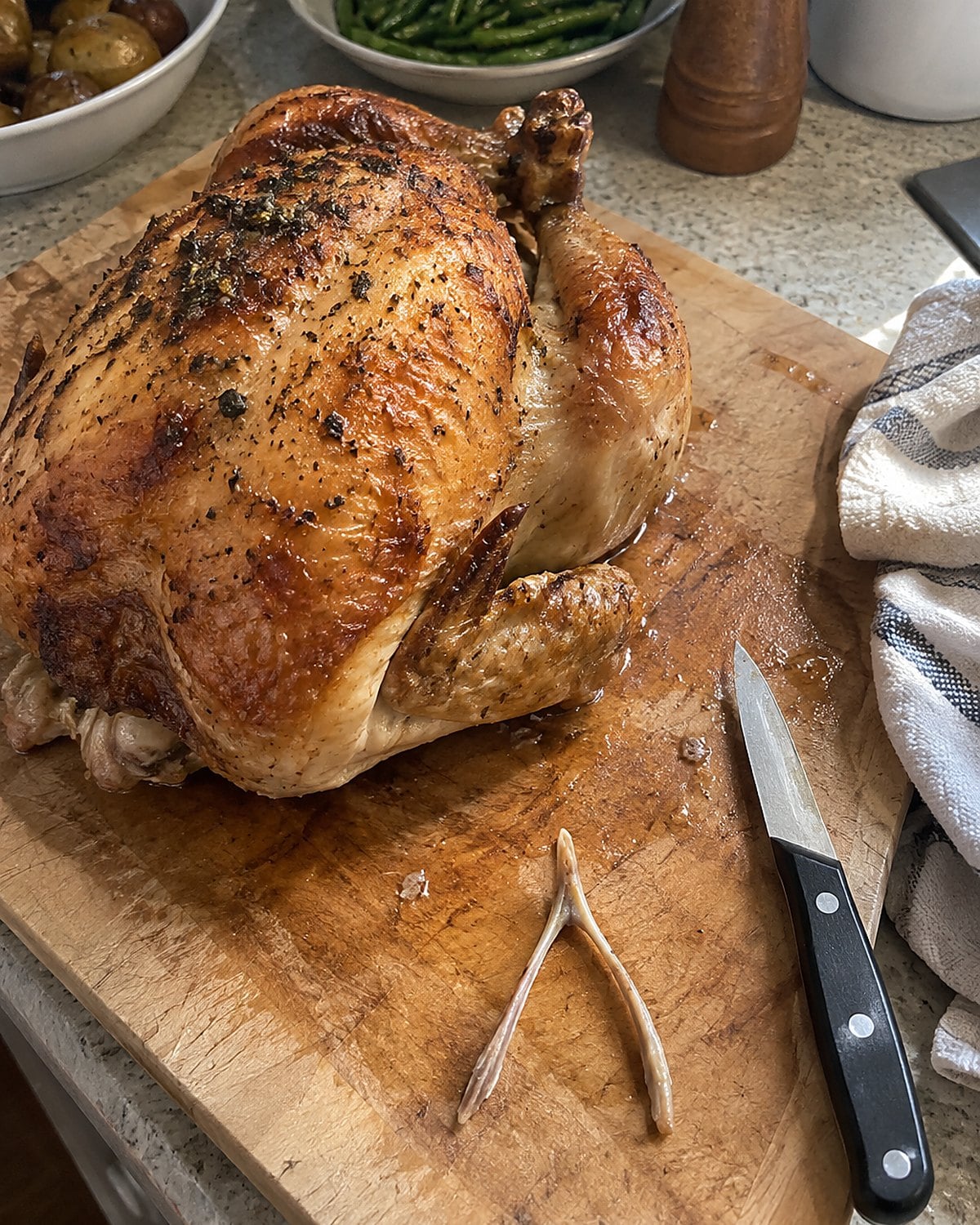 A small knife and a removed wishbone sit beside a whole chicken on a cutting board.