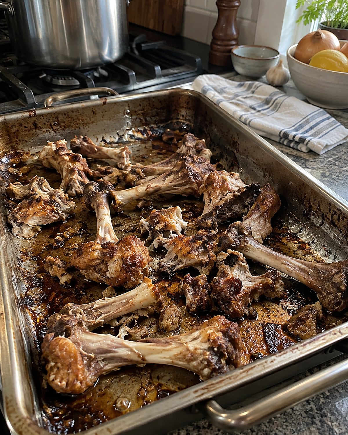 Browned chicken bones sit on a roasting pan, with a pot waiting on the stove.