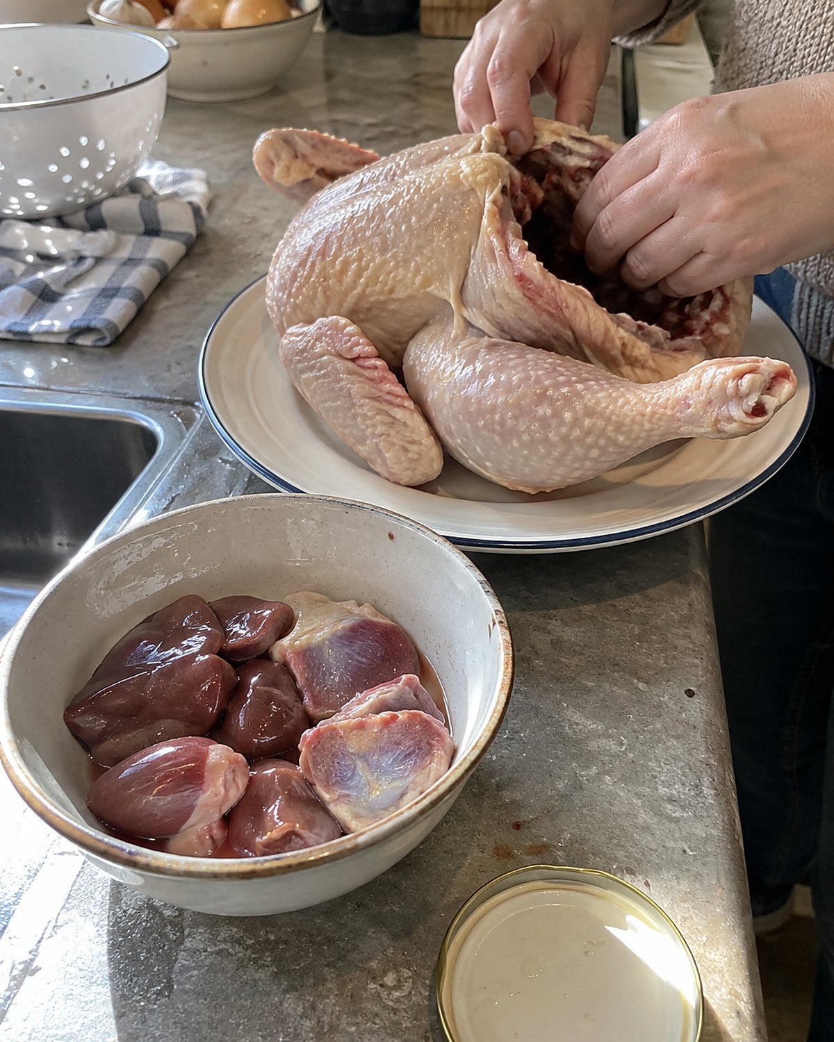 A small bowl holds chicken liver, heart, and gizzard beside an open whole chicken on the counter.
