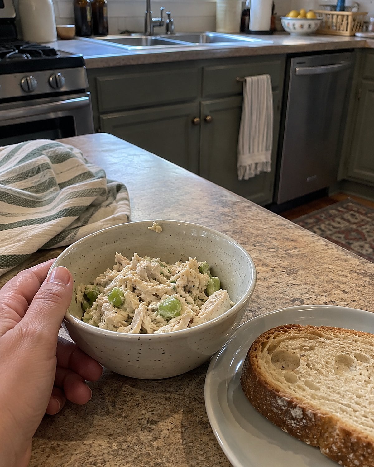 A small bowl of chicken salad with chopped celery sits beside a piece of bread.