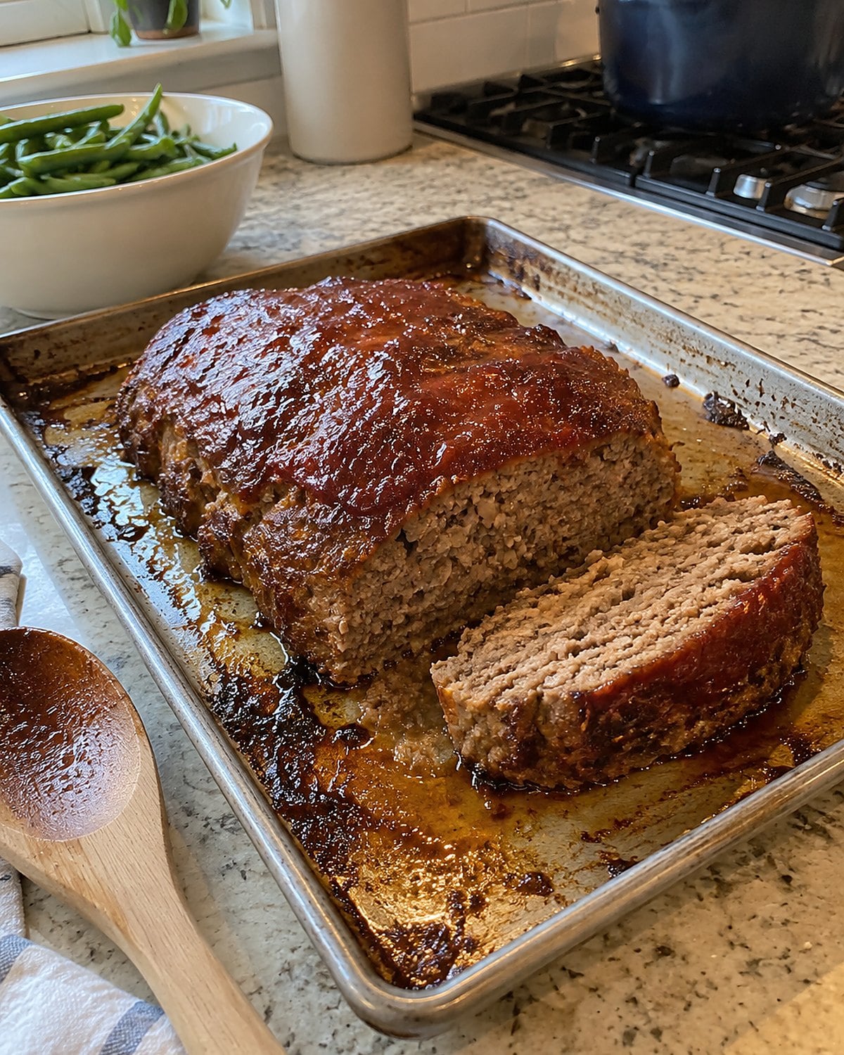 A free-form meatloaf on a rimmed sheet pan, with a slice cut and its browned side showing.
