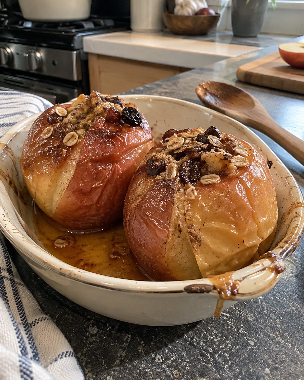 Two baked apples leaning in a small ceramic dish, their juices pooled at the bottom.