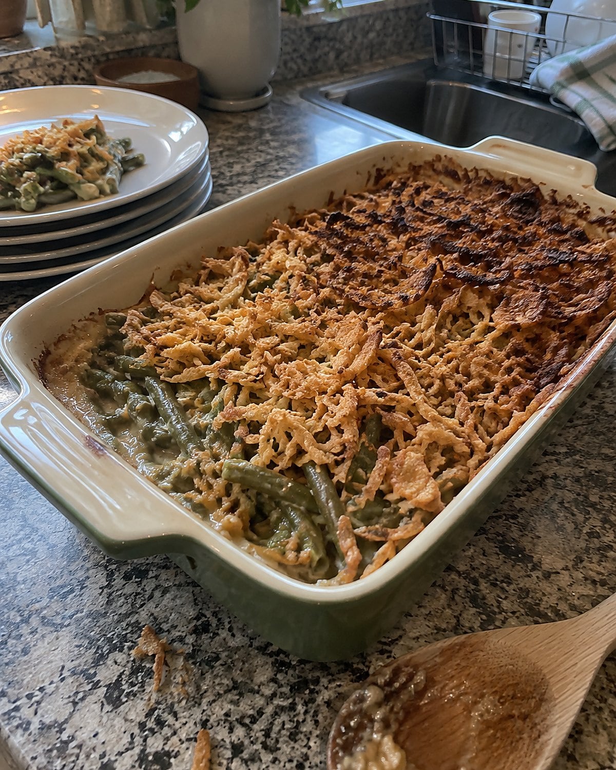 A shallow green bean casserole on a counter, its onion topping browned unevenly at the edges.