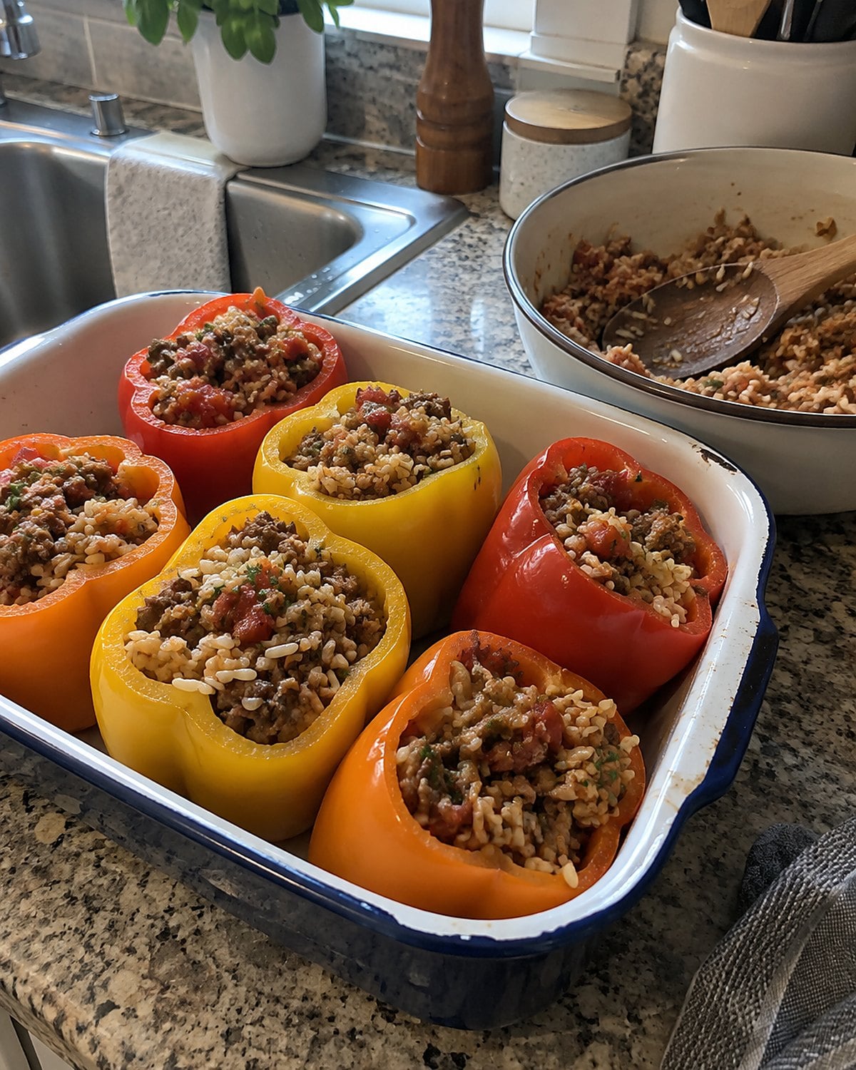 Bell peppers standing in a baking dish at the sink, with a bowl of cooked rice filling beside them.