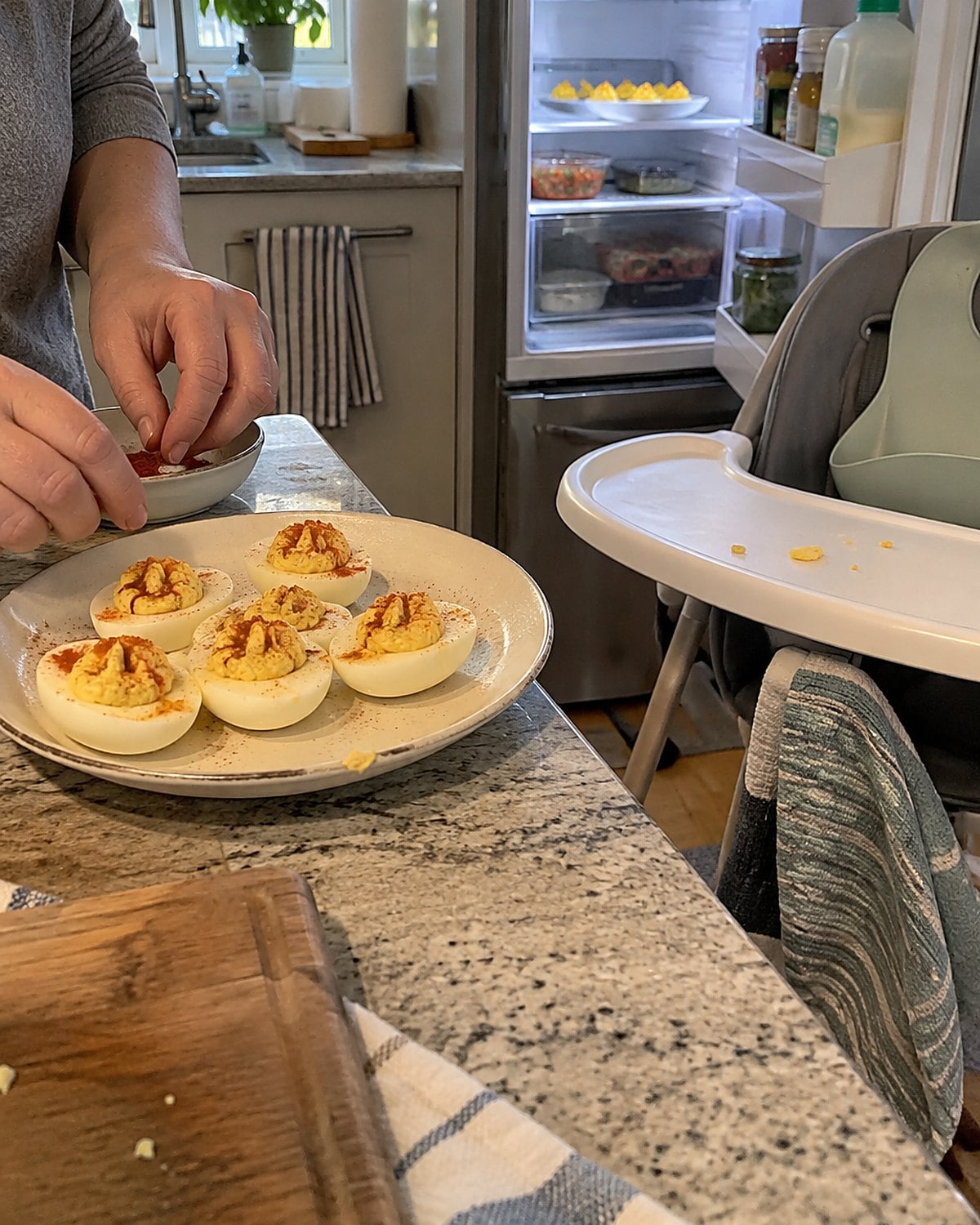 Deviled eggs on a small plate beside a grandchildโs high chair, with the remaining eggs visible in an open fridge.