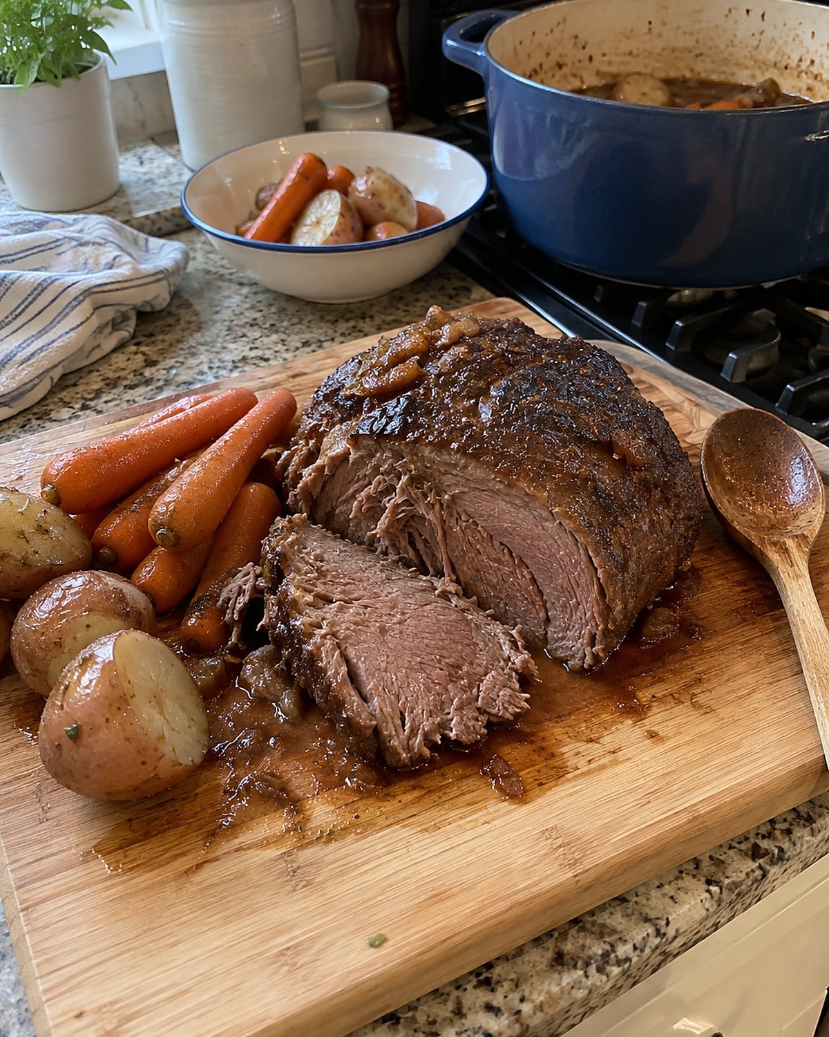 A pot roast on a cutting board beside intact carrots and potatoes lifted from the pot.