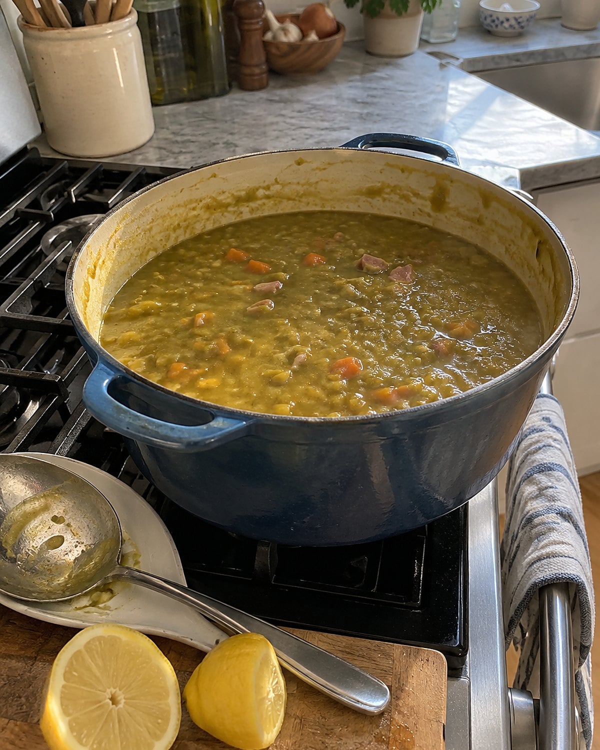 A pot of split pea soup beside a cut lemon and a soup spoon on the stove.