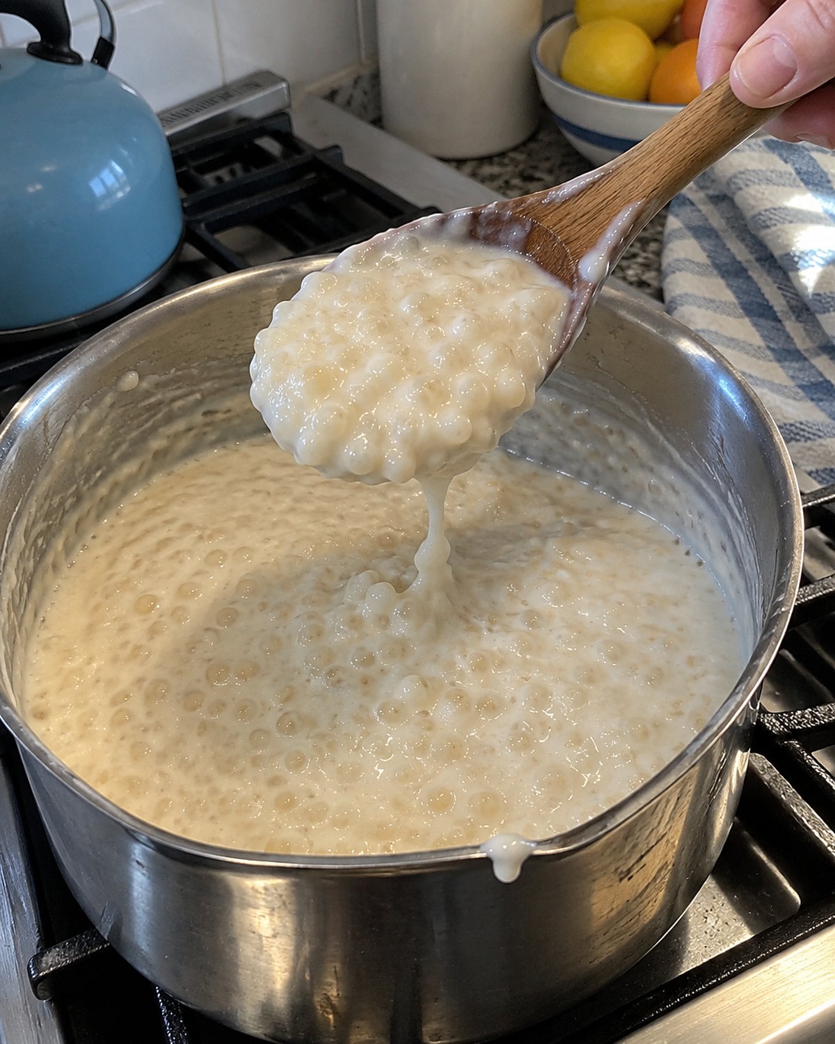 A wooden spoon lifts pearl tapioca pudding from a heavy saucepan on the stove.