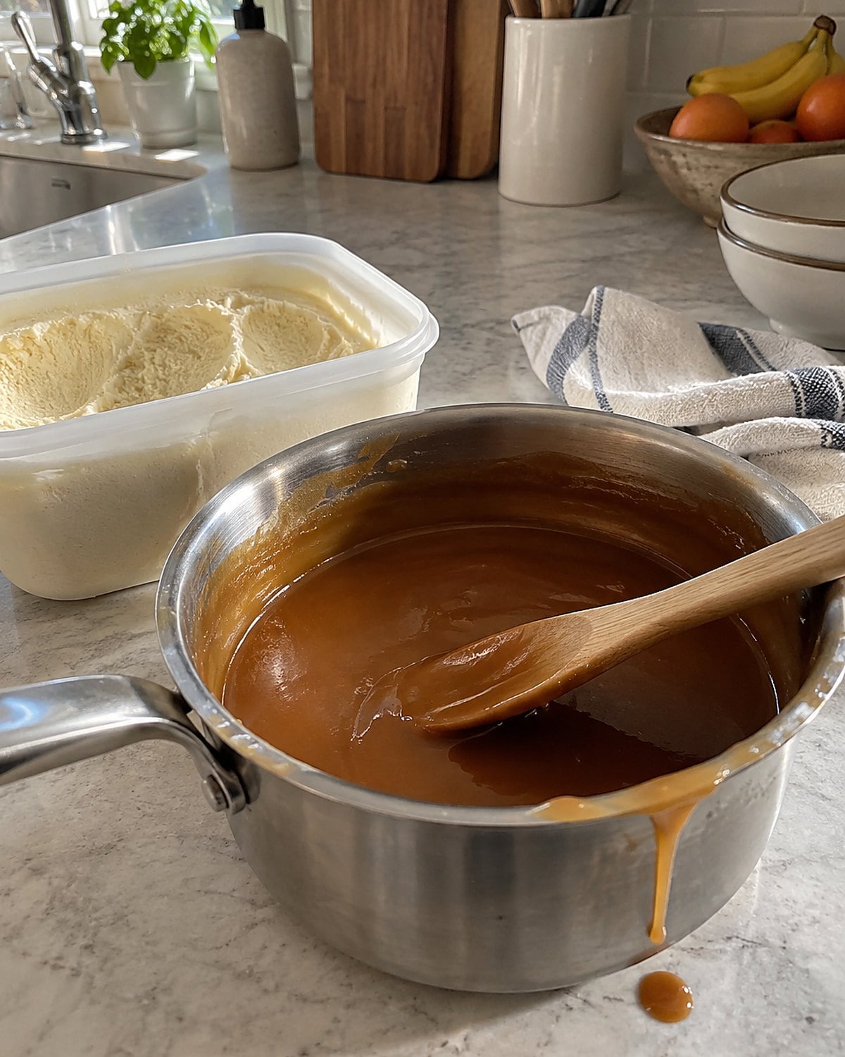 A small saucepan of butterscotch sauce sits beside an open carton of vanilla ice cream at the counter.