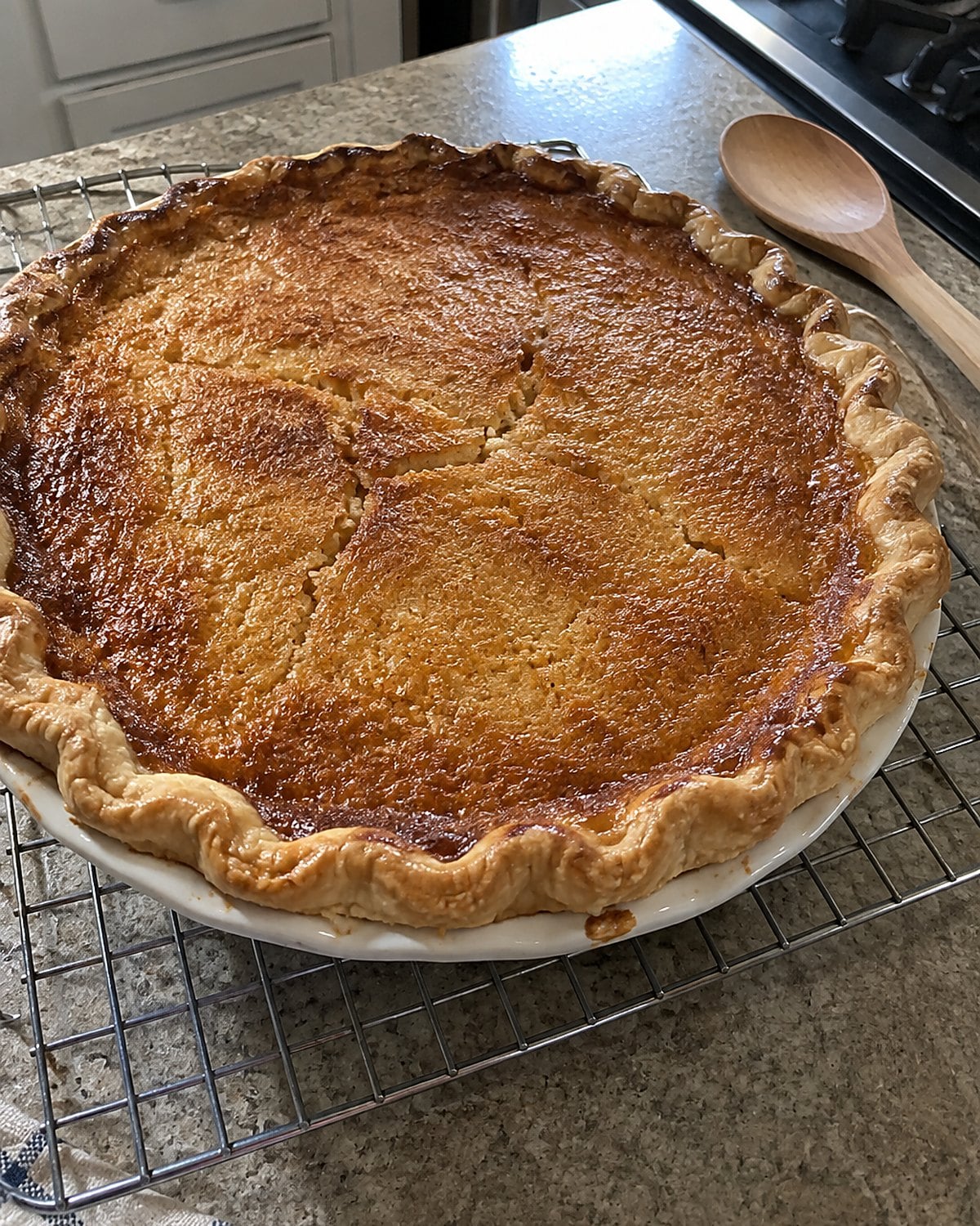 A chess pie with a browned, slightly cracked top cools on a wire rack near the stove.