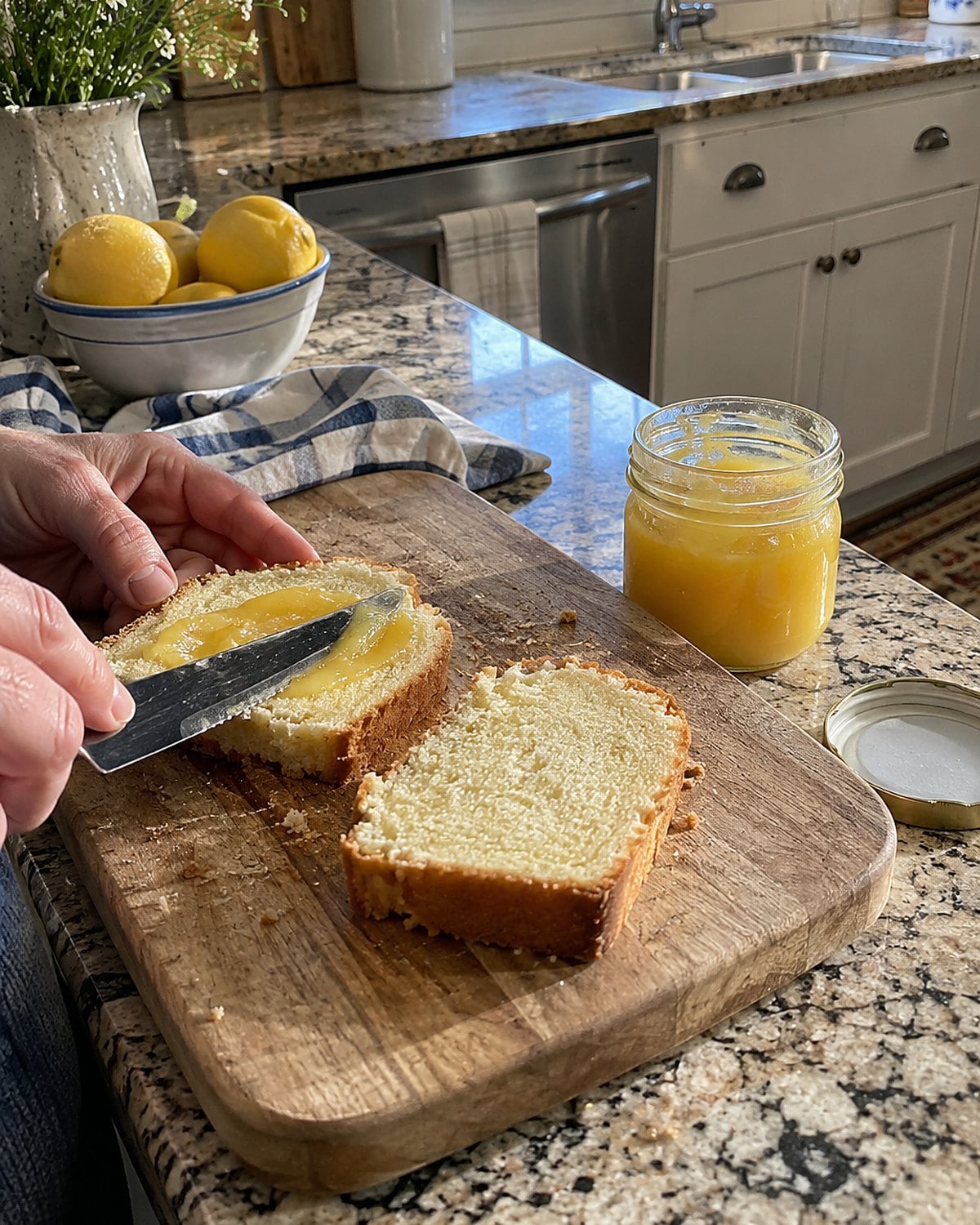 A small jar of lemon curd and two slices of pound cake sit beside a serrated knife.