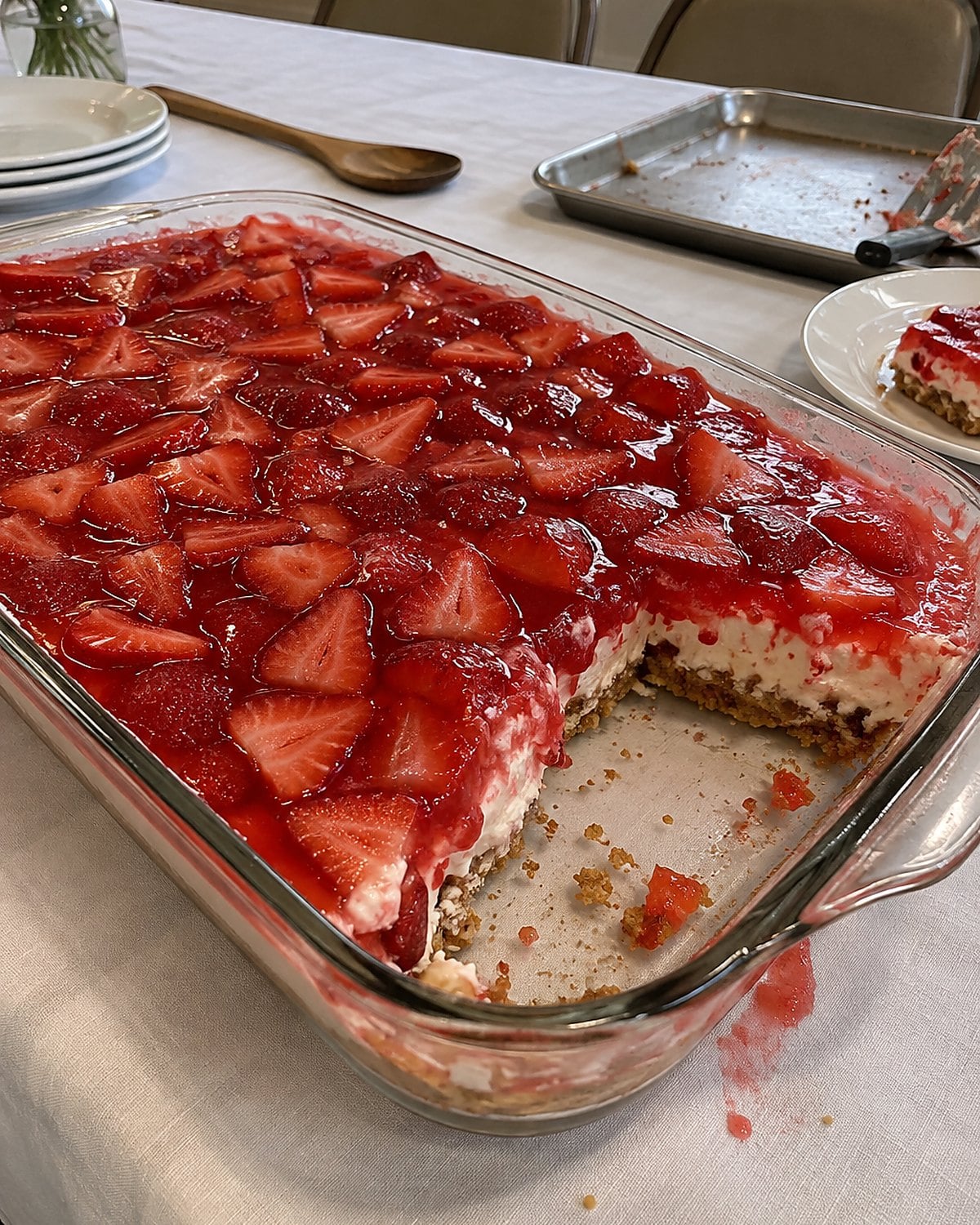 A glass pan of strawberry pretzel salad rests on a church hall table with one uneven square missing.