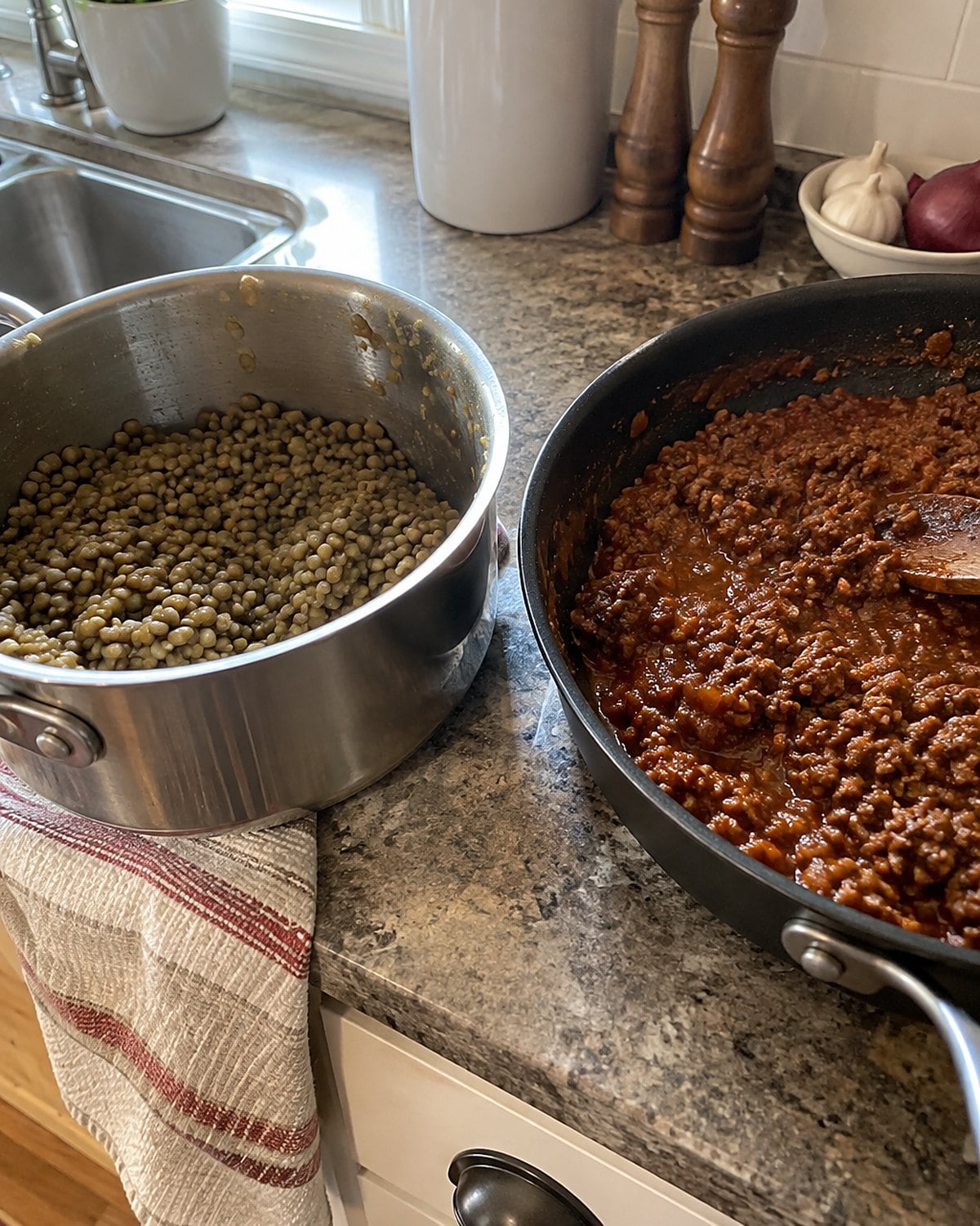 A pot of cooked lentils sits beside a skillet of sloppy joe filling on the counter.
