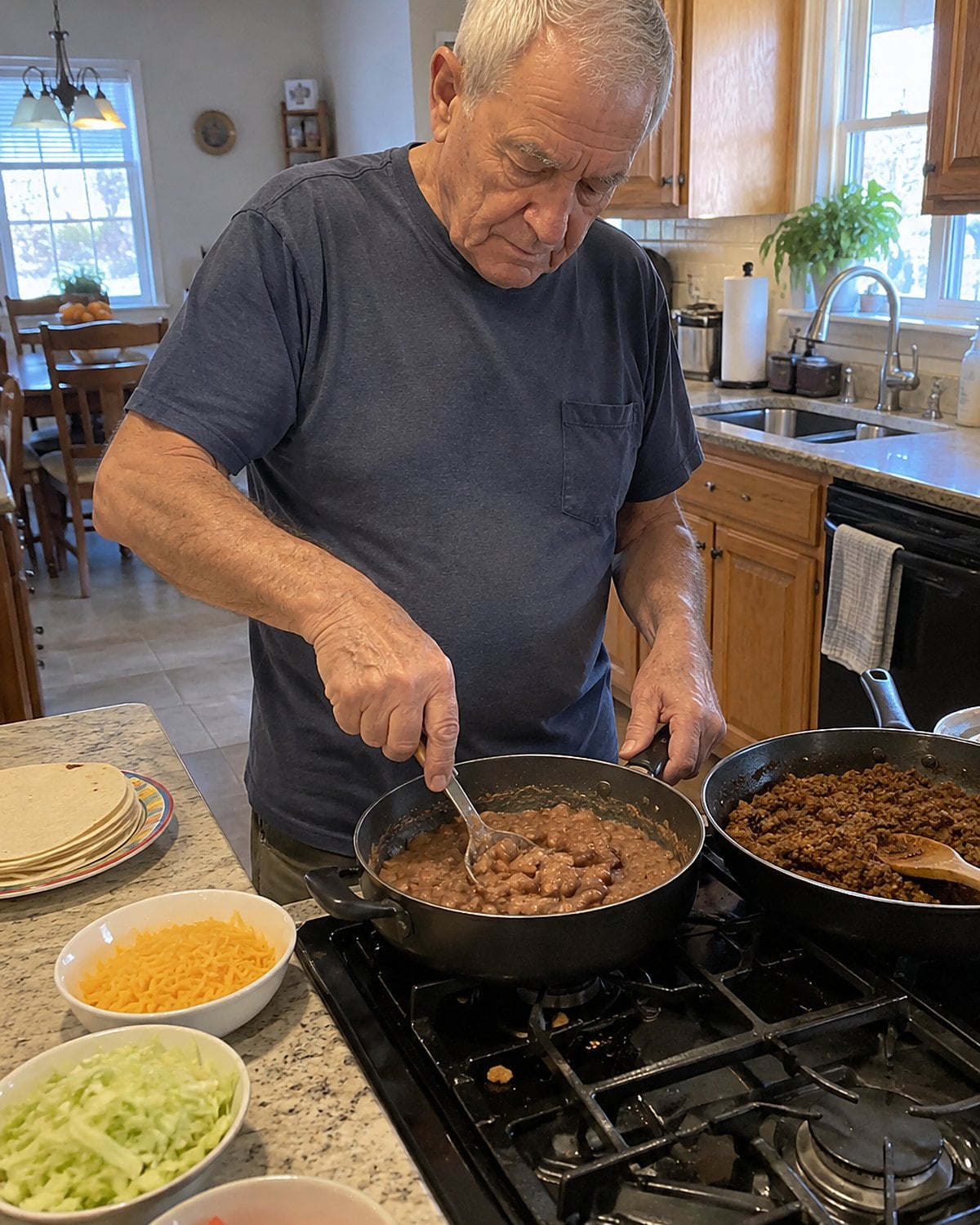 A hand mashes beans beside taco meat in a skillet on the stove.