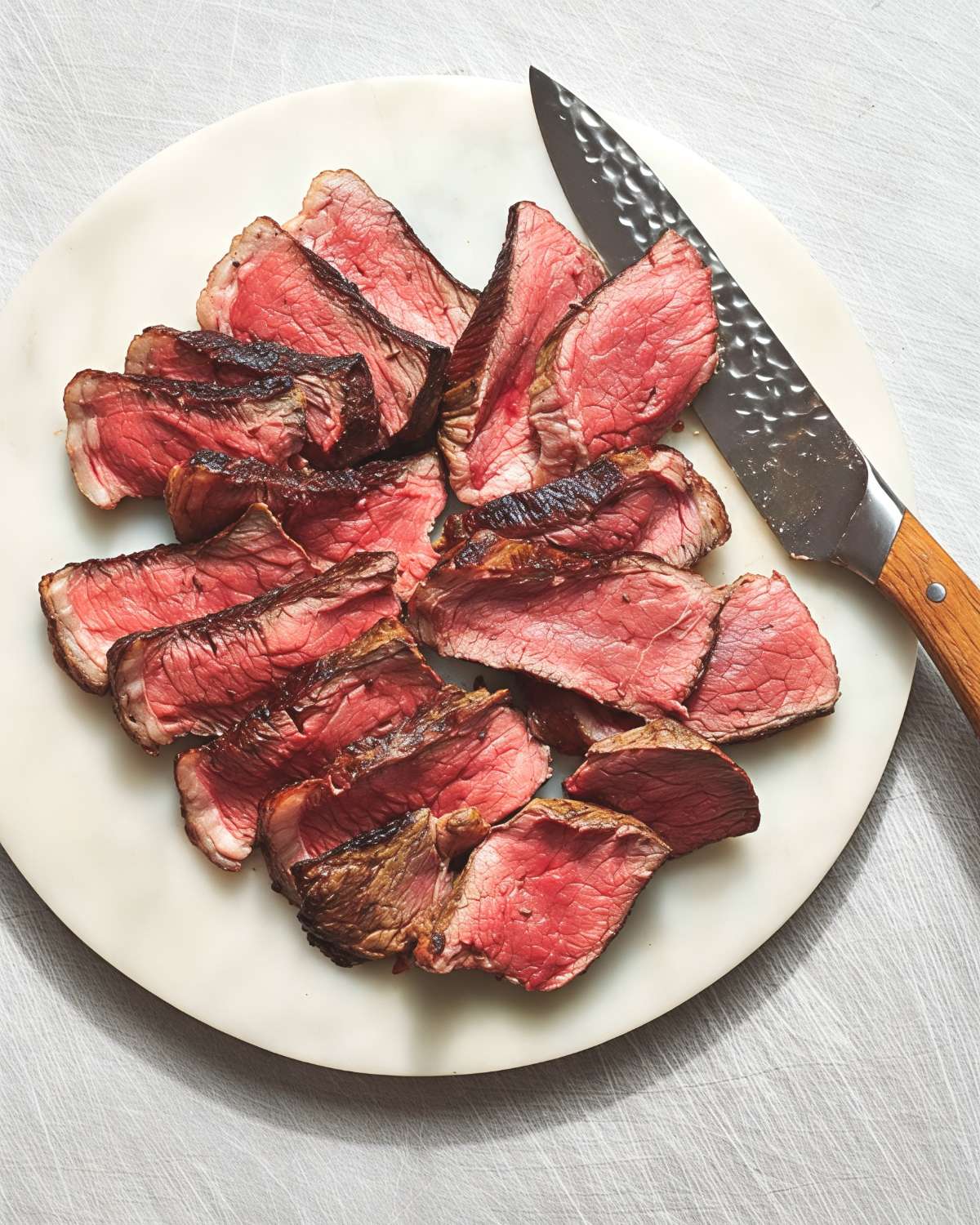 Perfectly seared and sliced tender Picanha Steak arranged on a white stone cutting board next to a wooden-handled knife, featured as a delicious high protein low carb recipes dinner.