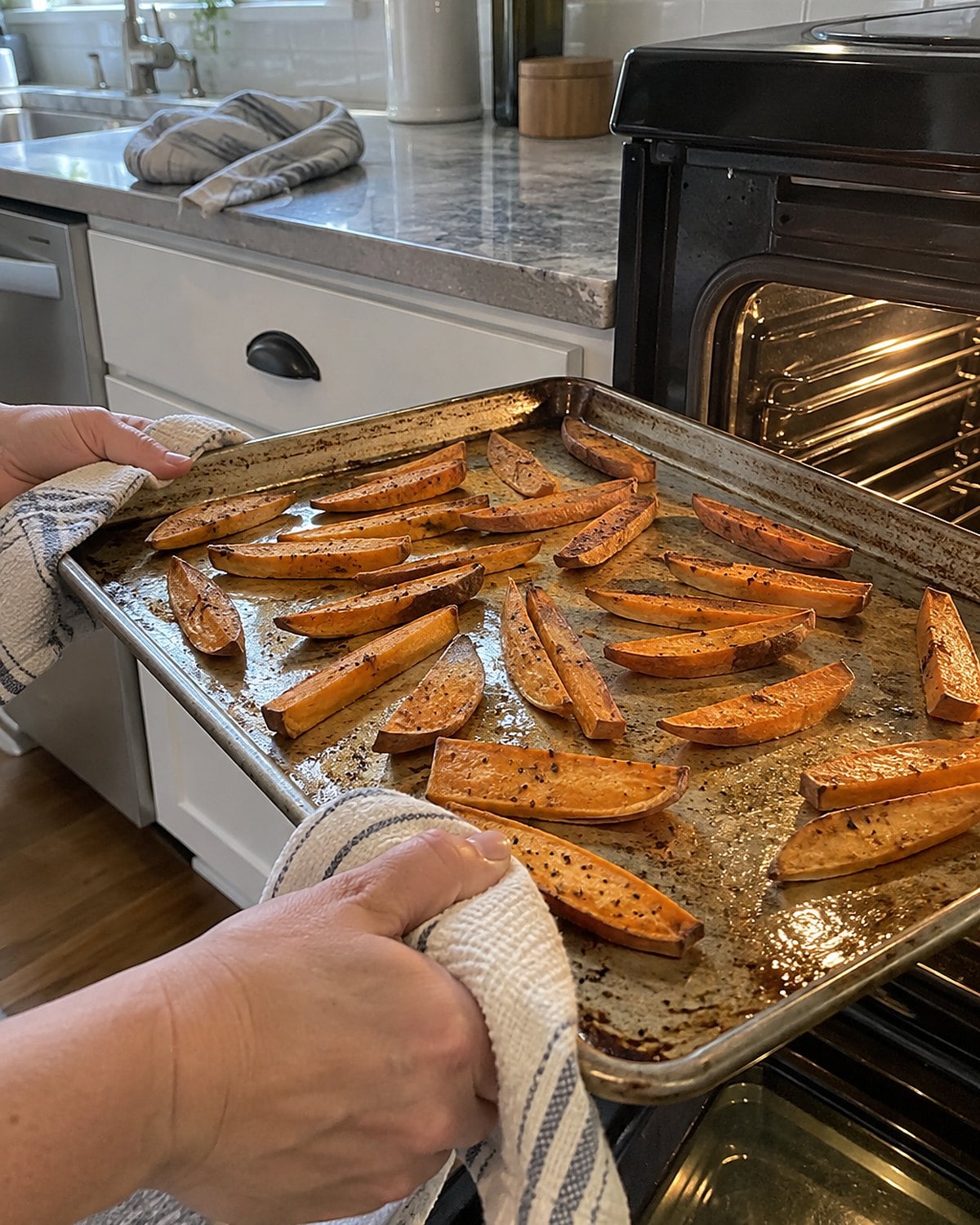 Sweet potato strips spread apart on a baking sheet near an open oven door.