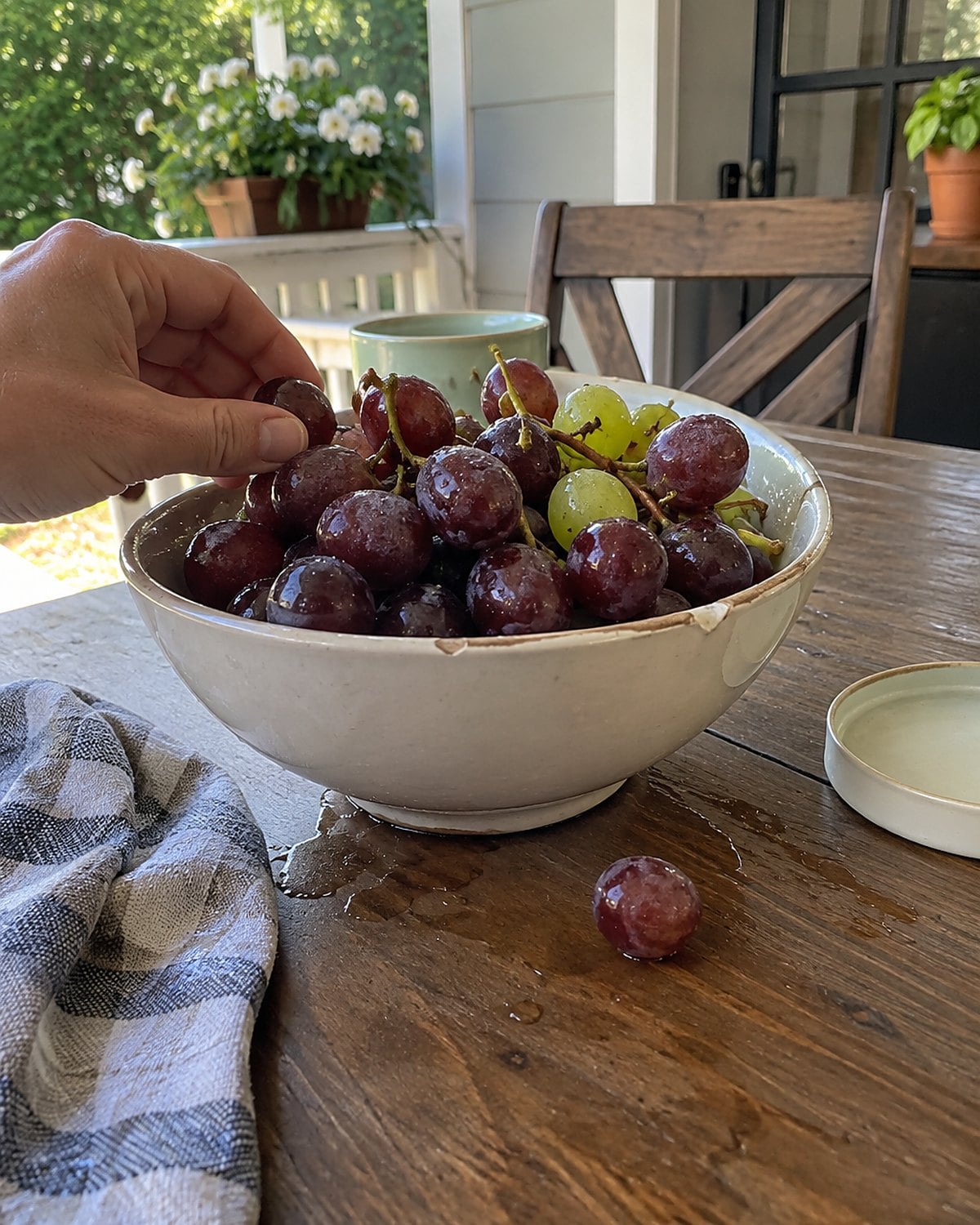 Chilled grapes in a bowl on a porch table beside a damp kitchen towel.