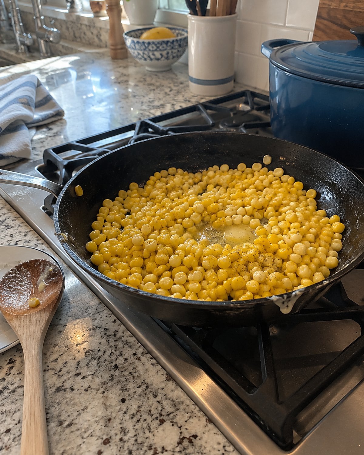 Buttered corn kernels in a skillet with a spoon resting beside it.