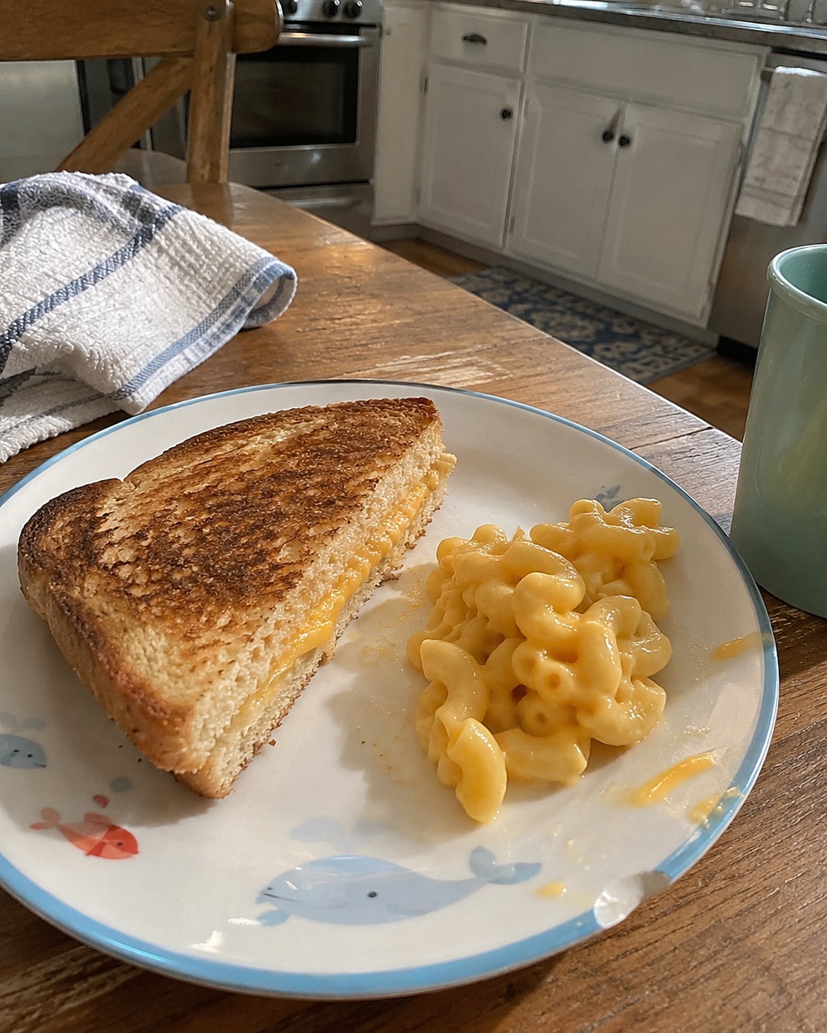A single spoonful of macaroni and cheese beside a sandwich on a child's plate.