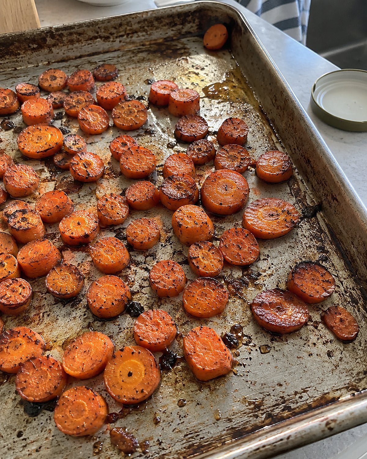 Carrot coins with browned edges spread across a worn baking sheet.