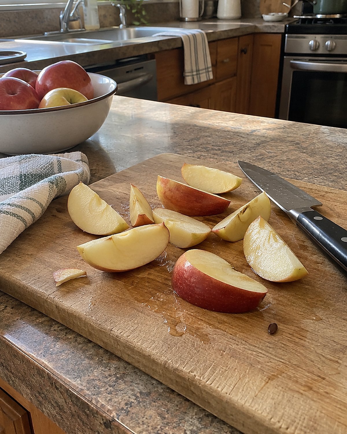 Uneven apple wedges on a kitchen counter beside a knife and a folded dish towel.