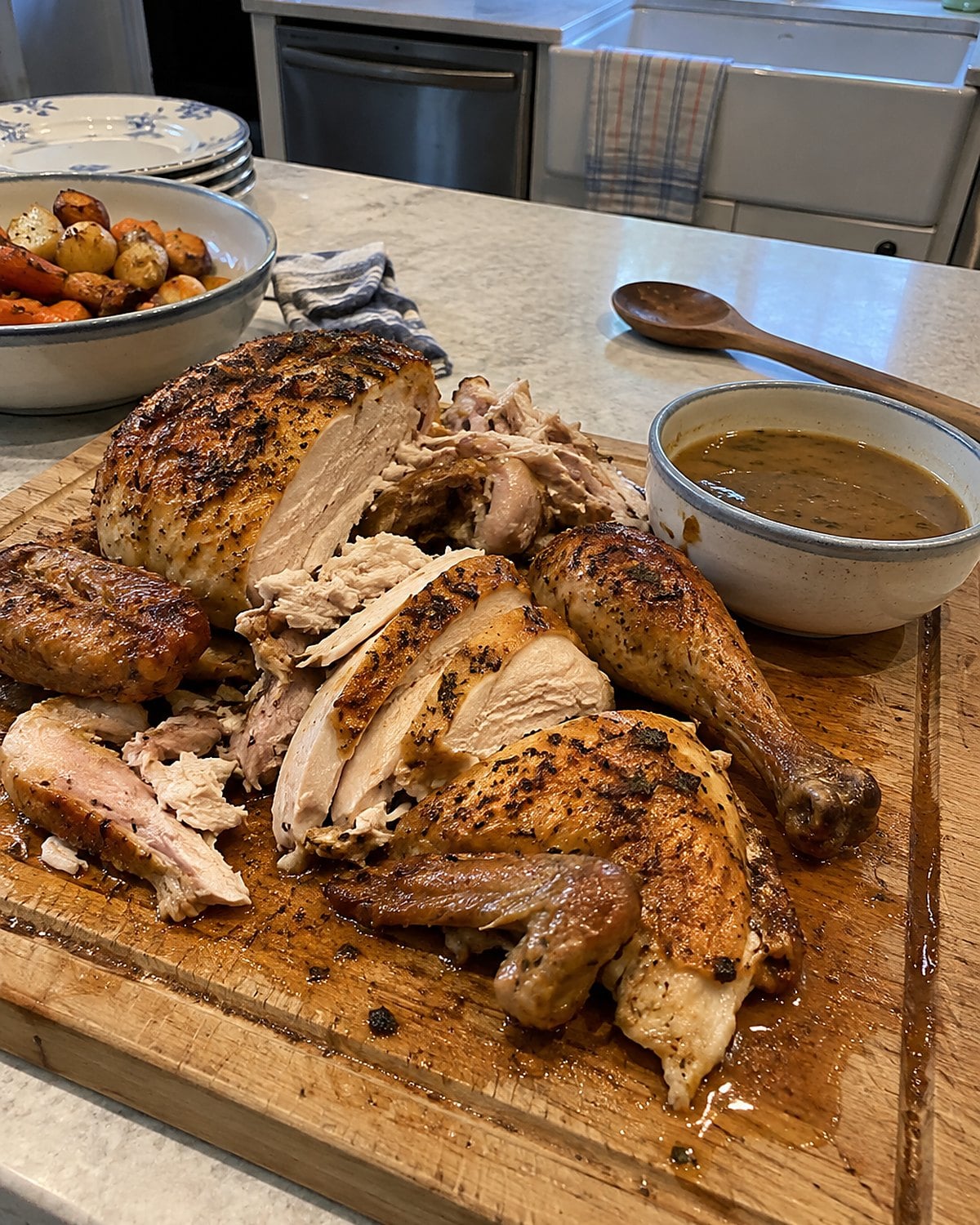Carved roast chicken on a board with a small bowl of gravy beside it.