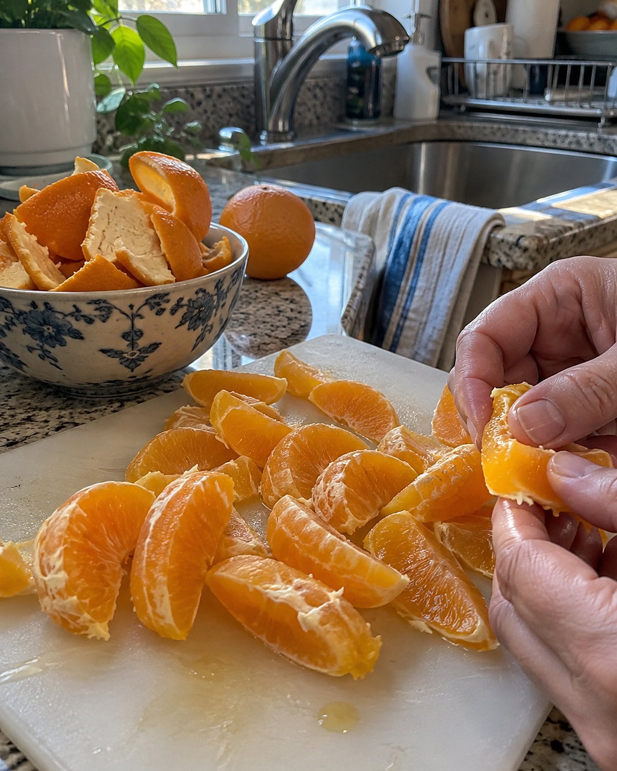 Peeled orange wedges beside a bowl of peels near the sink.