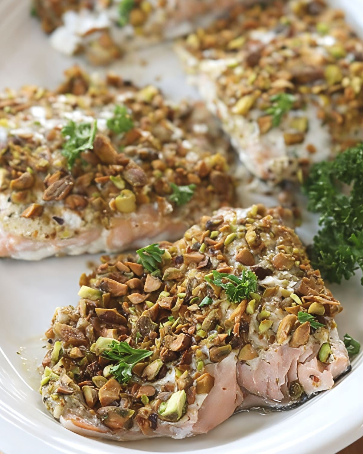 Close-up view of flaky tender Pistachio Crusted Salmon coated in golden roasted chopped pistachios and garnished with parsley sprigs, featured as a delicious high protein low carb recipes dinner.