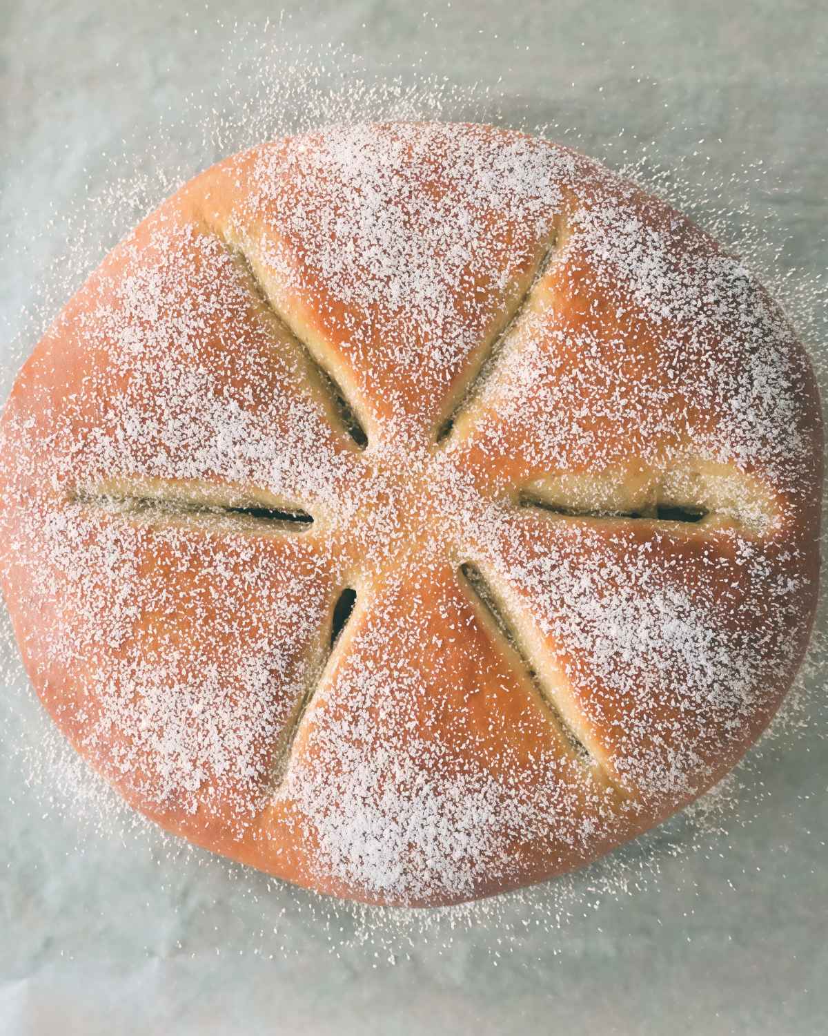 A golden round Pompe à l'Huile olive oil sweet bread with decorative slash cuts and a dusting of powdered sugar, prepared as a traditional European Christmas dessert.