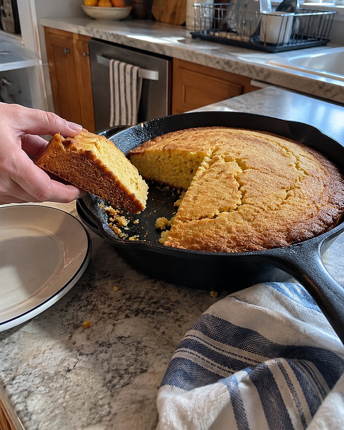 A cast-iron skillet of cornbread on the counter, with one rough-edged slice cut from it.