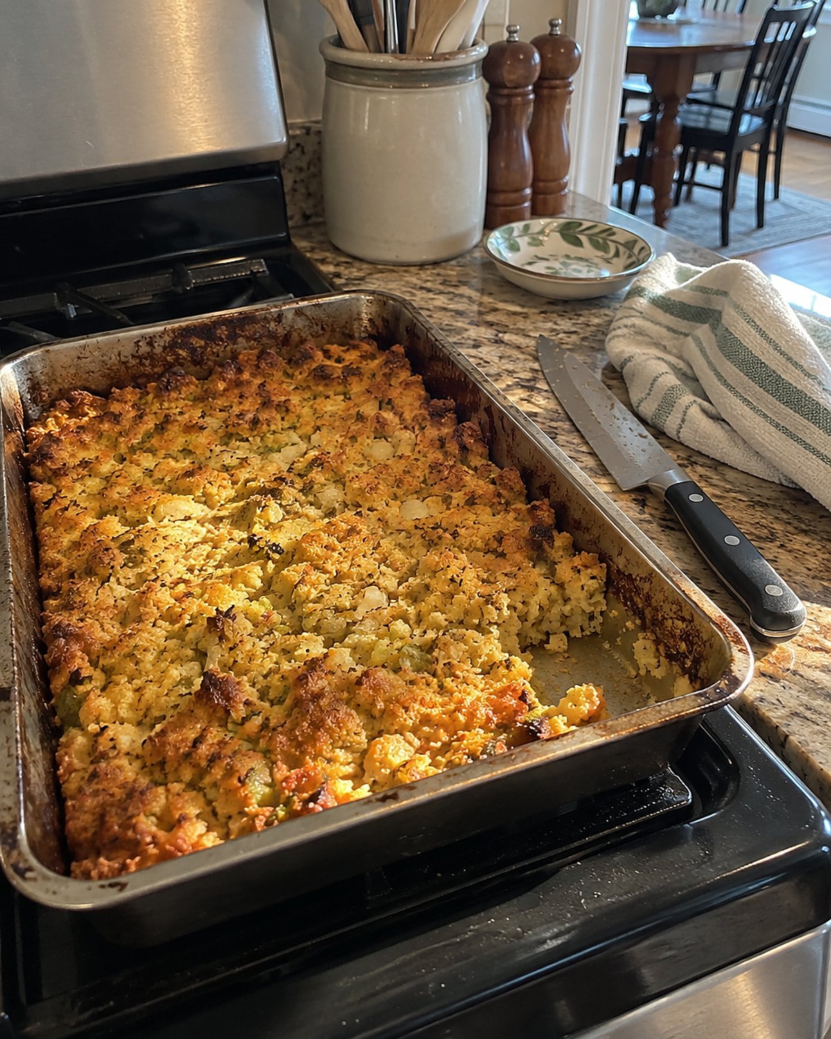 A shallow pan of cornbread dressing on the stove, with browned edges and a knife resting beside it.