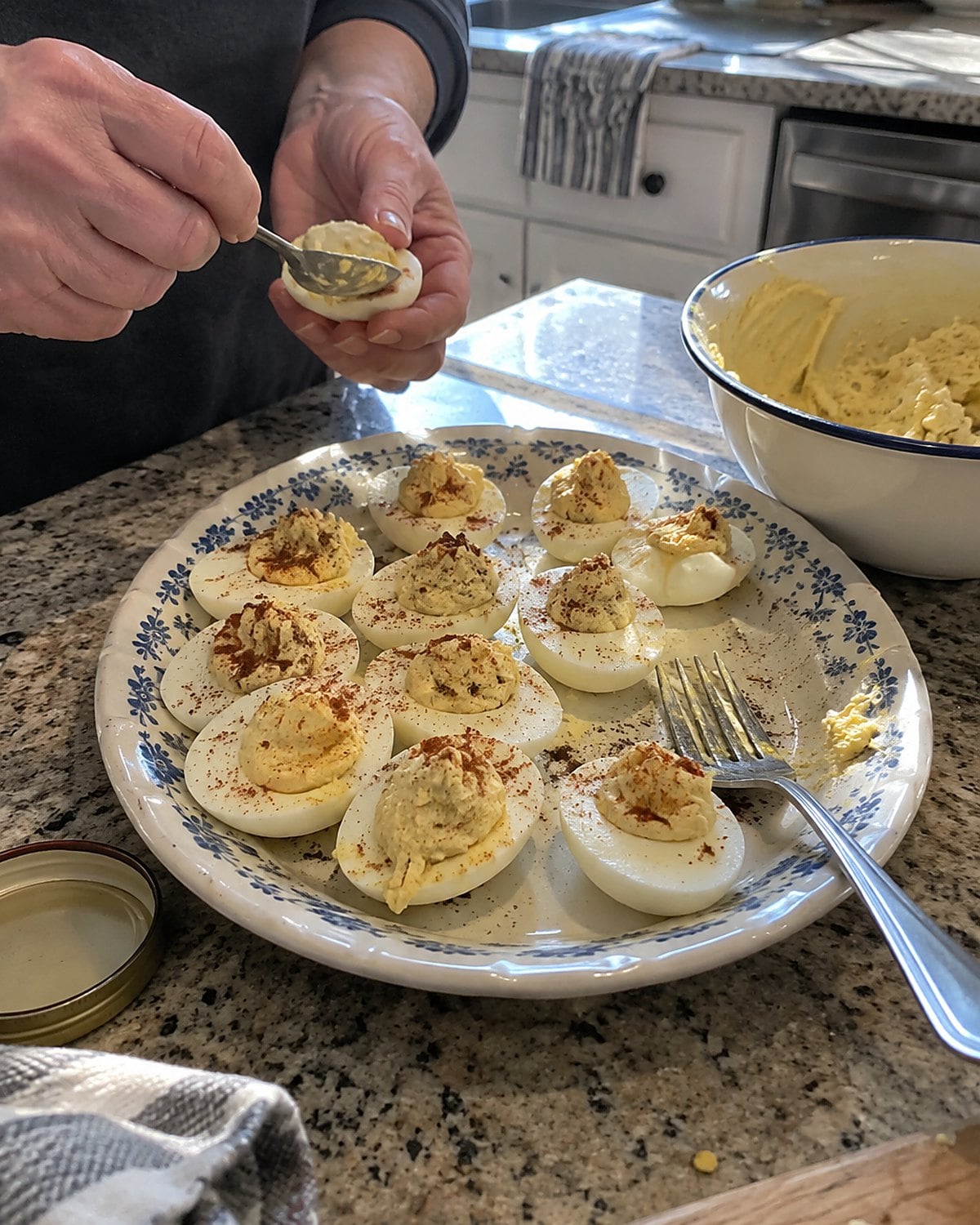 Egg halves on a worn kitchen platter beside a fork and a bowl of thick yolk filling.