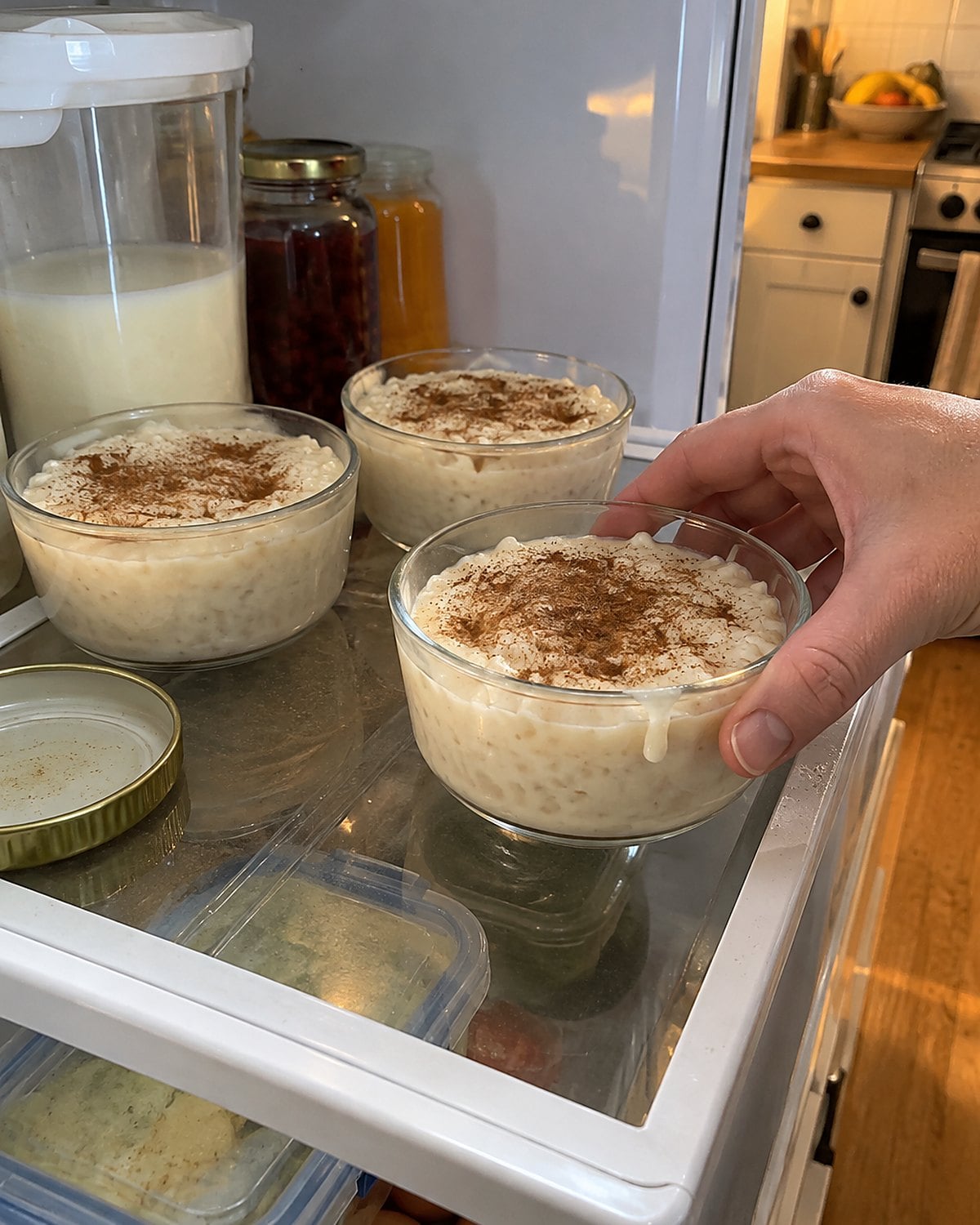Small cups of rice pudding lined up inside a refrigerator, with cinnamon on their surfaces.