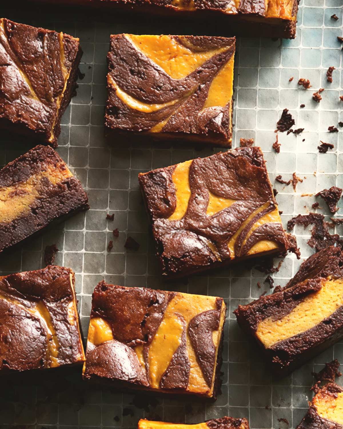 Square slices of fudgy chocolate brownies swirled with orange pumpkin cheesecake batter are arranged on parchment paper.