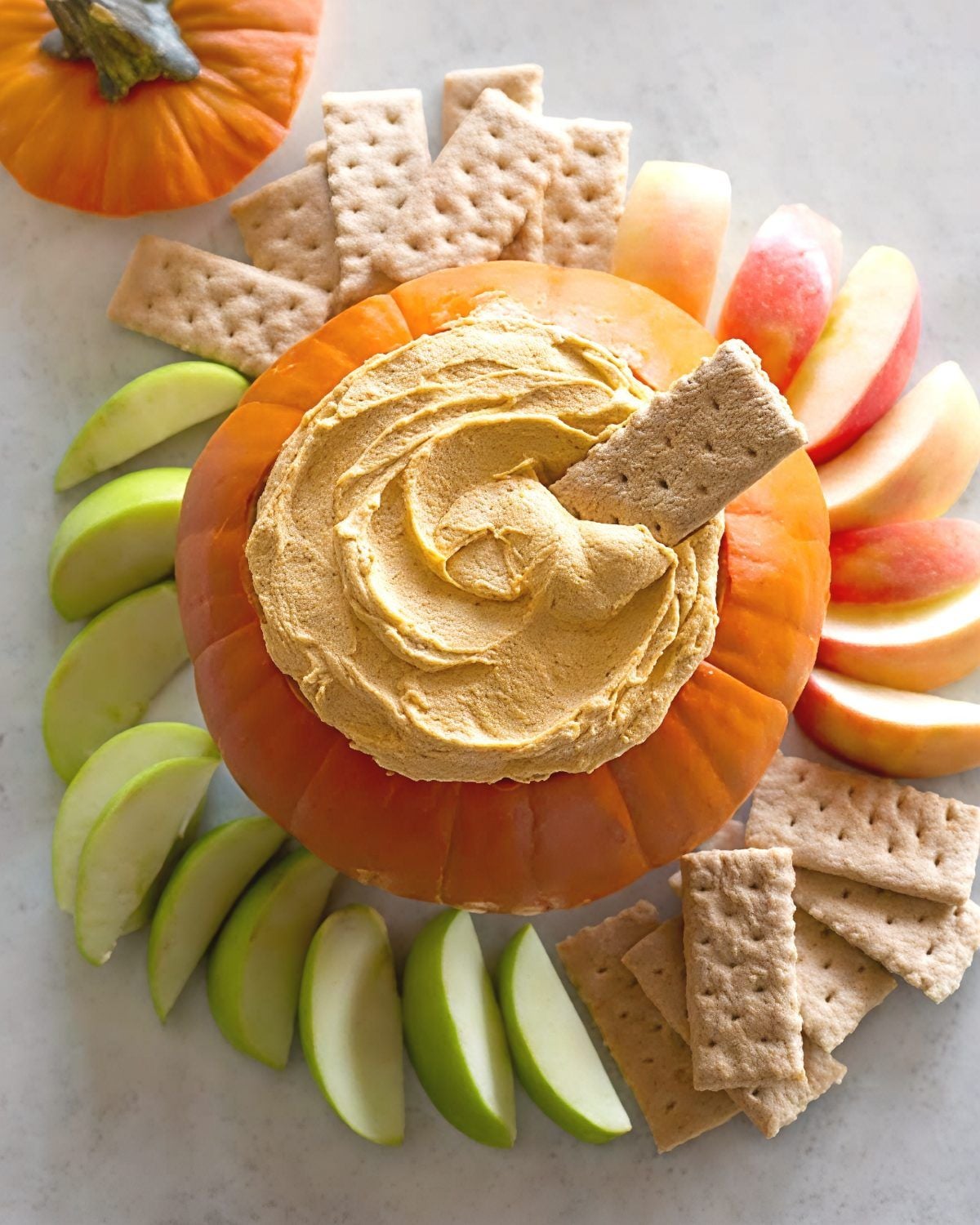 Creamy pumpkin fluff dip served inside a hollowed-out pumpkin surrounded by graham crackers and fresh apple slices, perfect for Thanksgiving side dishes for a crowd.