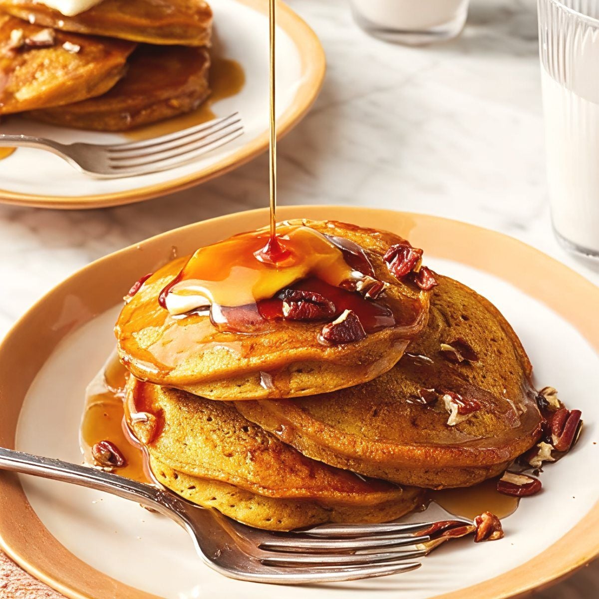 A stack of fluffy pumpkin pancakes topped with butter and pecans with maple syrup pouring down as Thanksgiving breakfast ideas