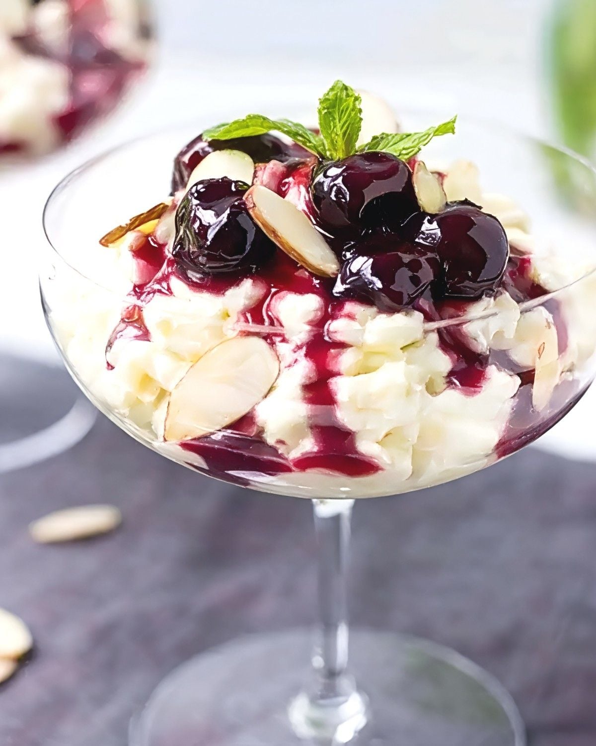 Traditional Danish Risalamande rice pudding served in a glass dish topped with dark cherry sauce, sliced almonds, and a mint sprig as a classic European Christmas dessert.